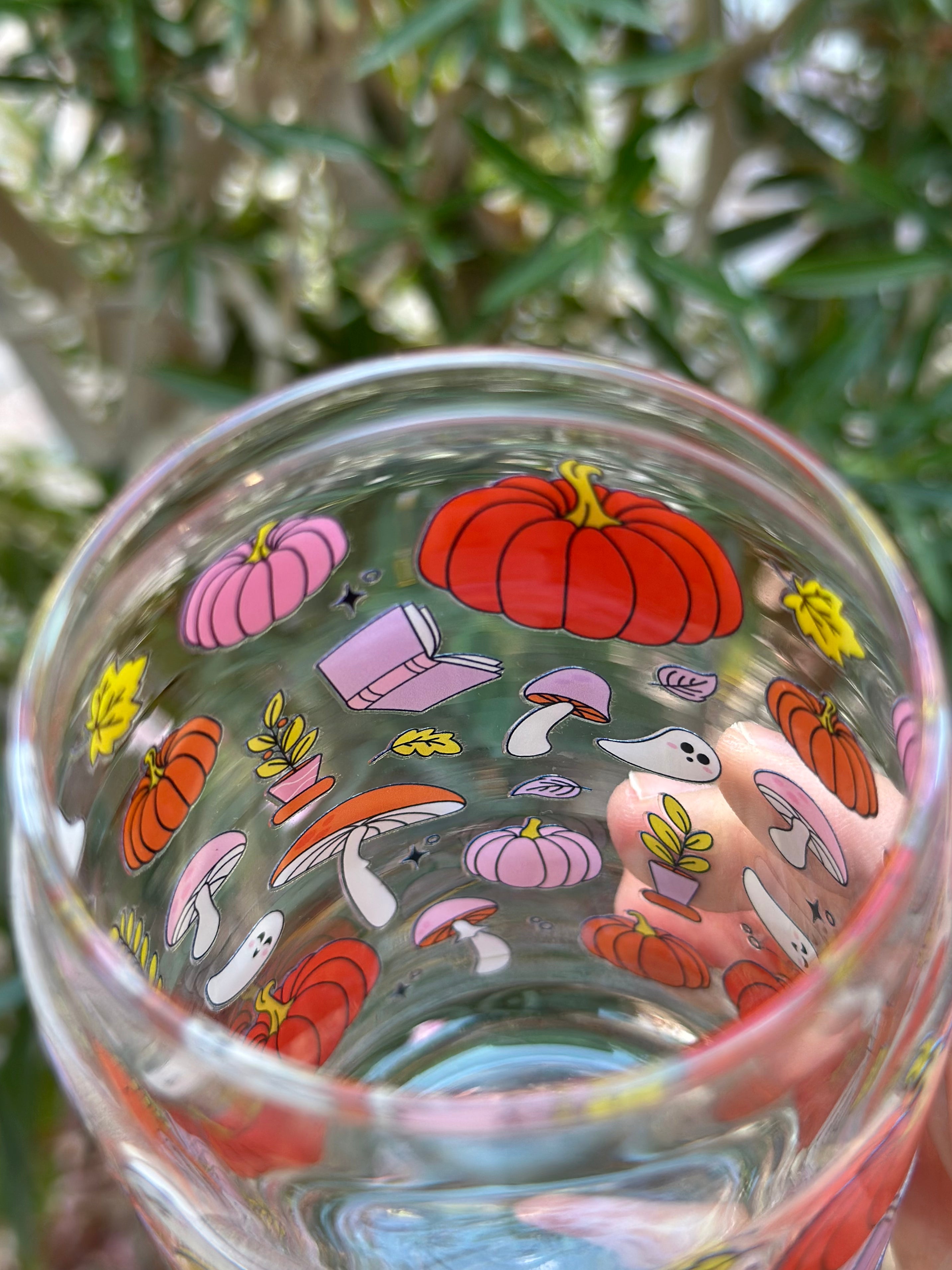 Inside view of glass can cup showing colorful pumpkin, ghost, mushroom, and book designs for a cozy Halloween aesthetic.