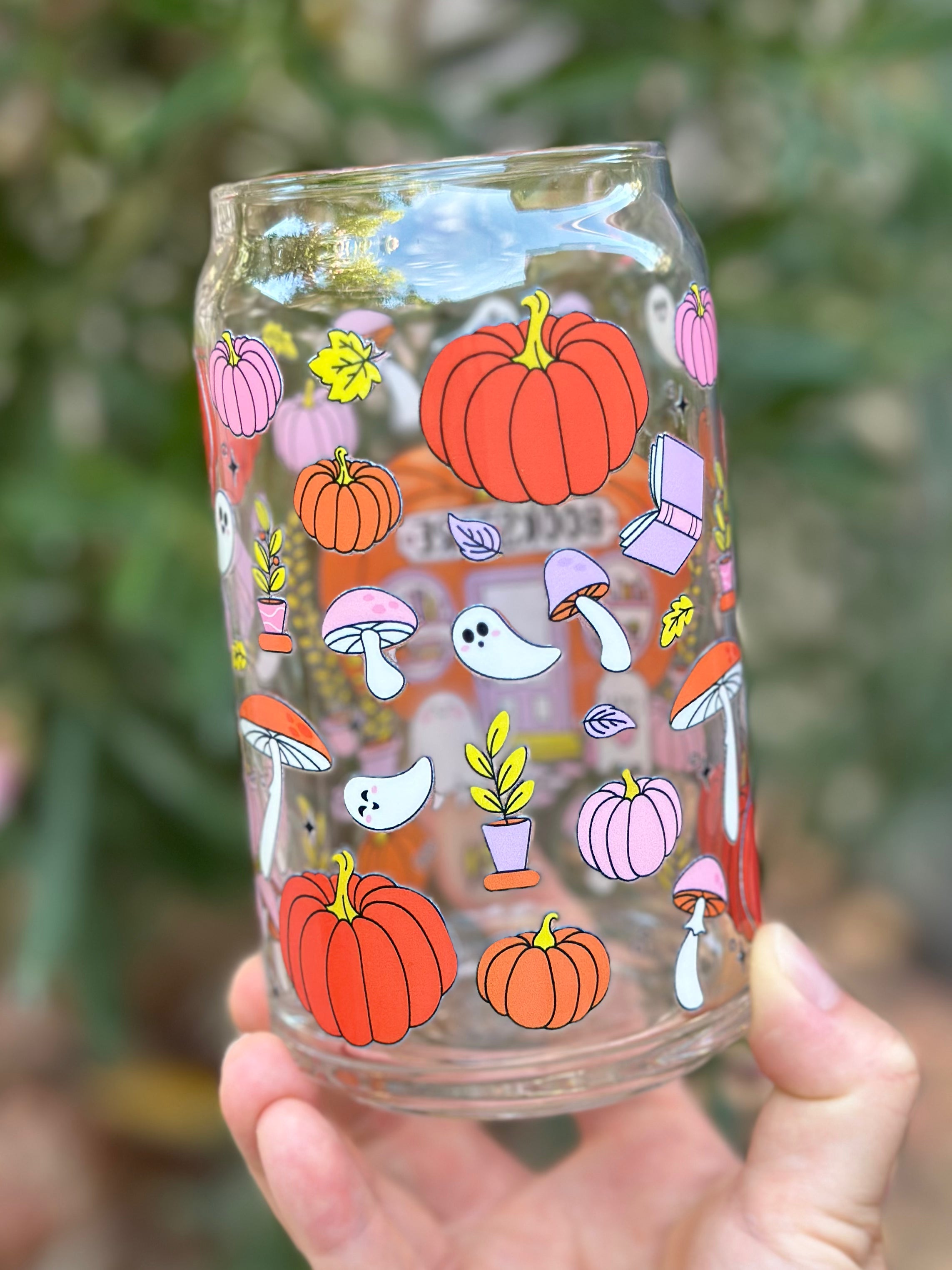 Back view of fall-themed glass can cup decorated with pumpkins, ghosts, mushrooms, plants, and leaves in orange, pink, and yellow tones.