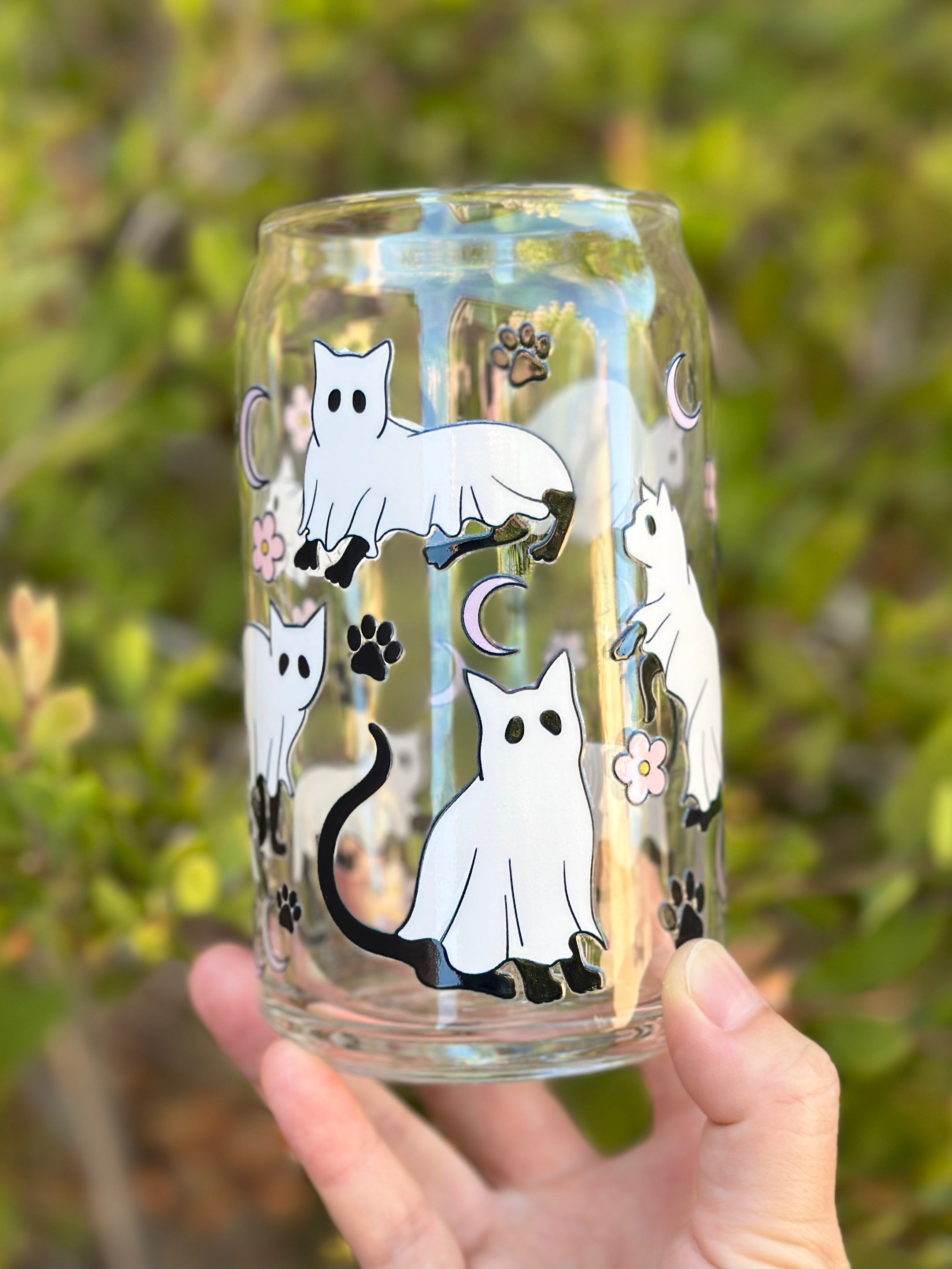 Glass can cup featuring sitting and walking ghost cats, black paw prints, moons, and pink flowers.