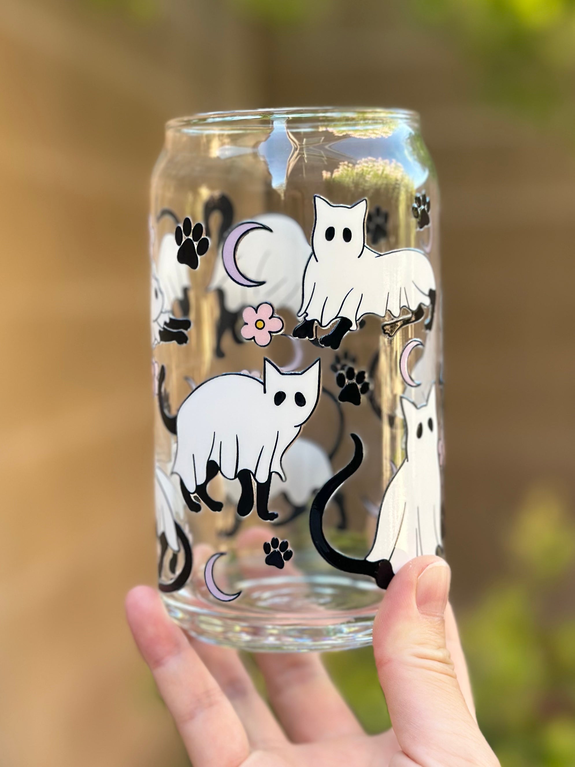 Clear glass can cup with playful black cats dressed as ghosts, pink flowers, paw prints, and crescent moons.