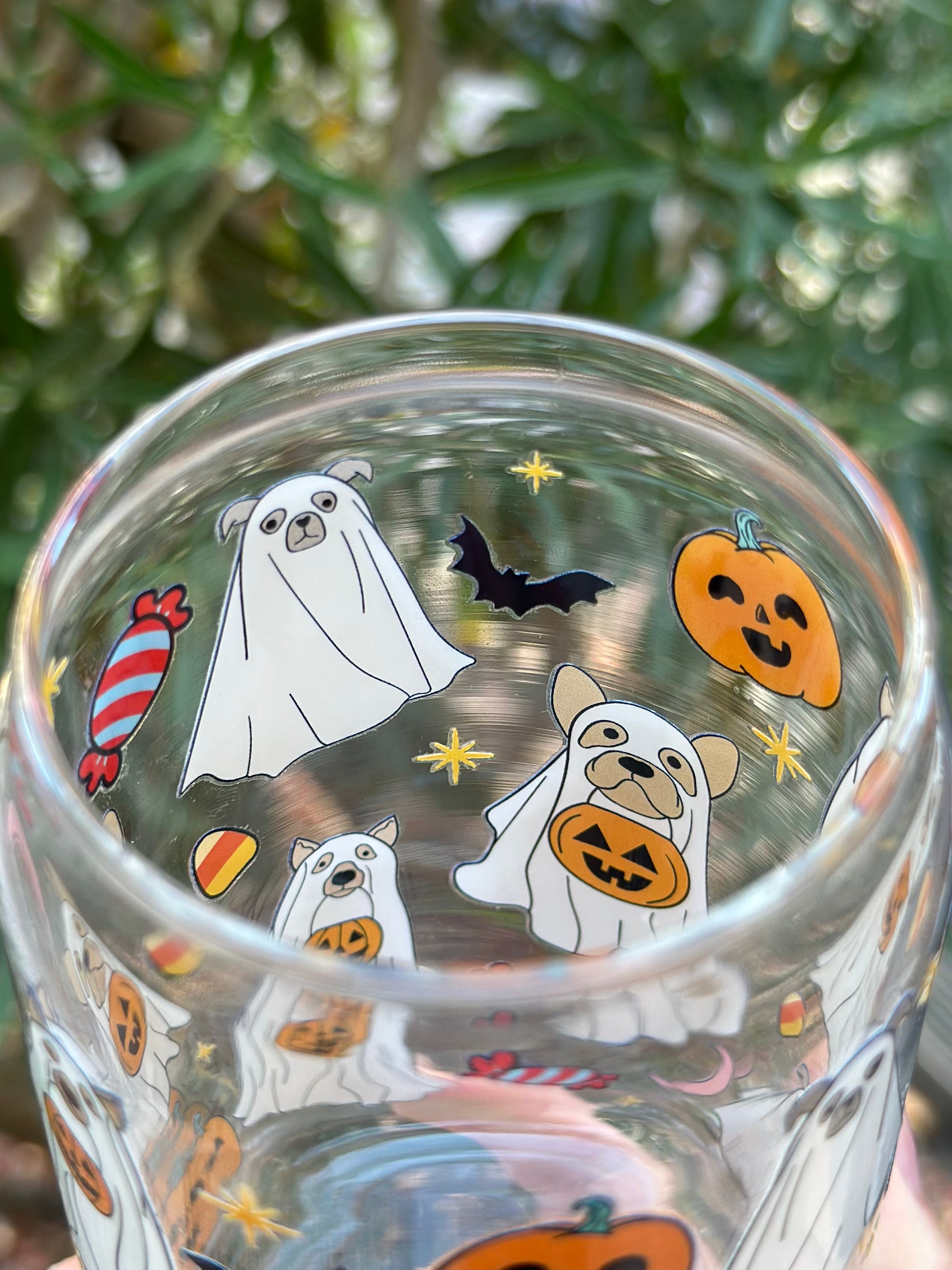 Inside view of clear glass can cup decorated with dogs in ghost costumes holding jack-o’-lanterns, surrounded by pumpkins, bats, stars, and candy.