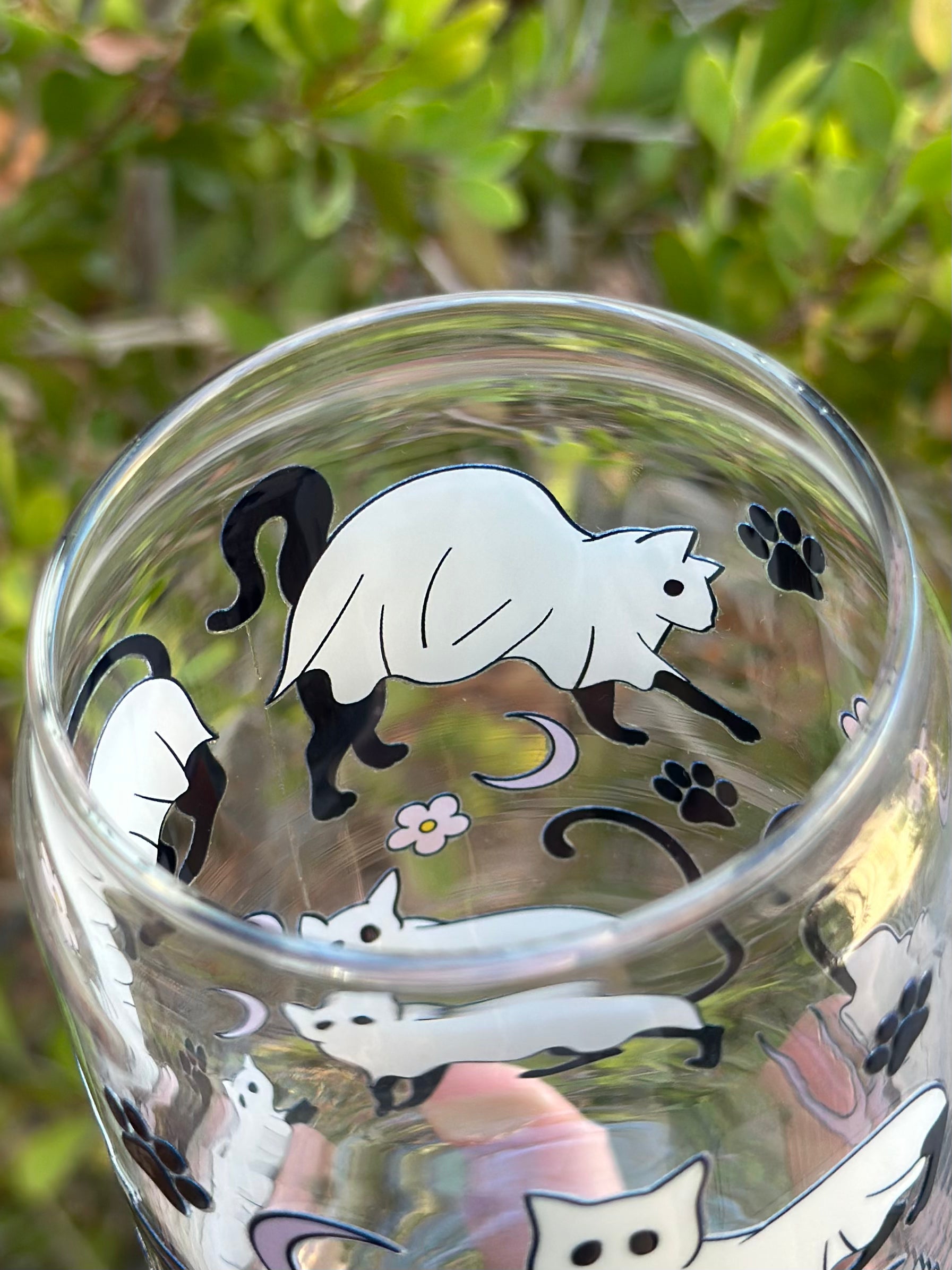 Inside view of glass can cup with black cat in a ghost costume, surrounded by paw prints, crescent moons, and pink flowers.