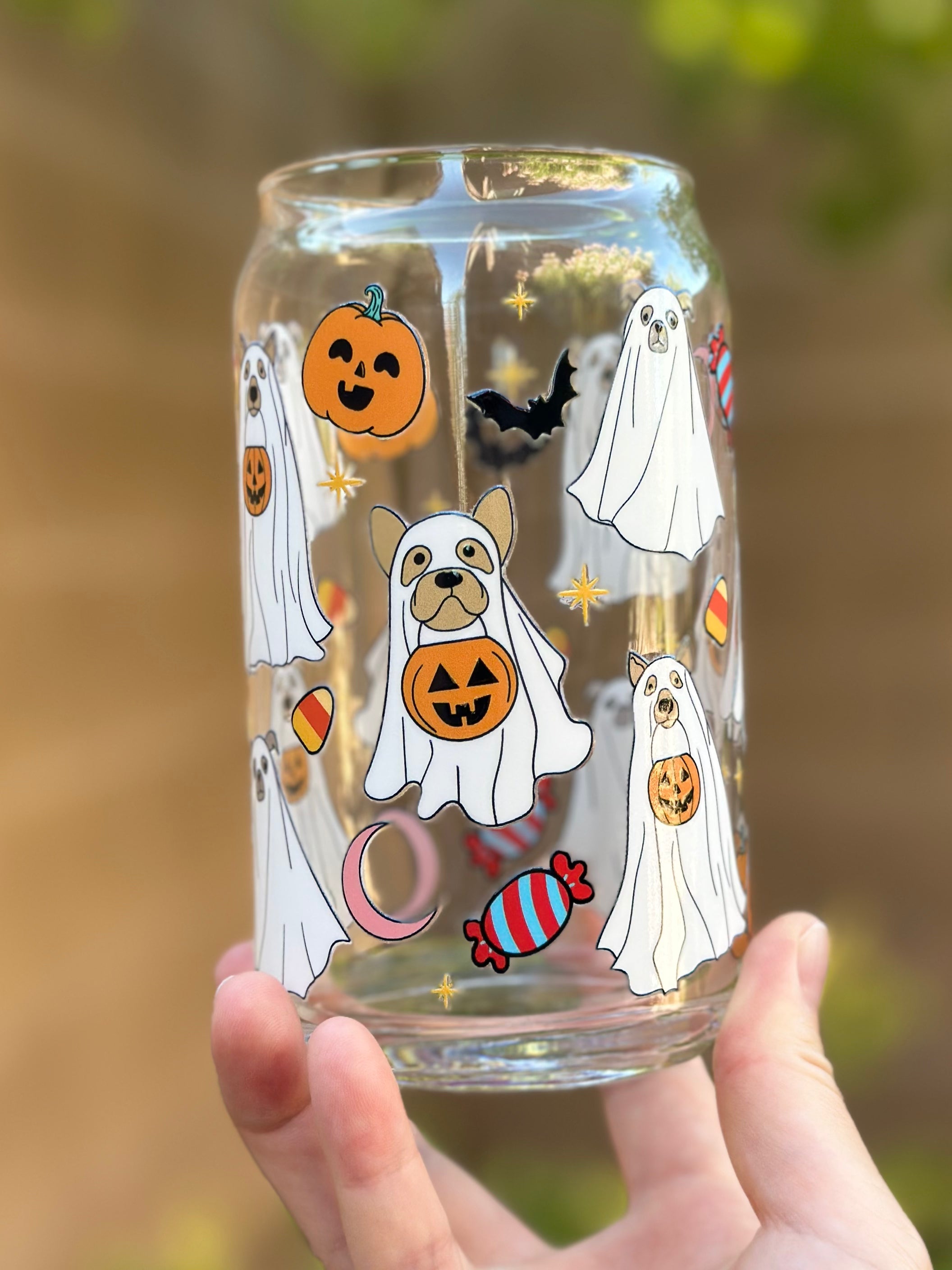 Clear glass can cup with playful ghost dog illustrations, smiling pumpkins, candy pieces, bats, and stars on a festive Halloween background.