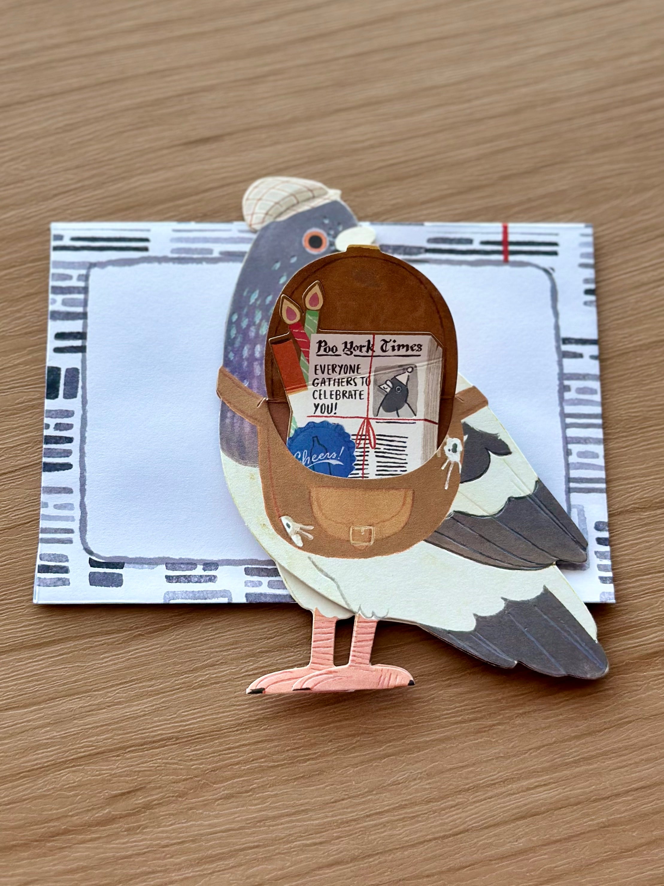 Interactive pigeon card with messenger bag opened to reveal “Poo York Times” newspaper message.