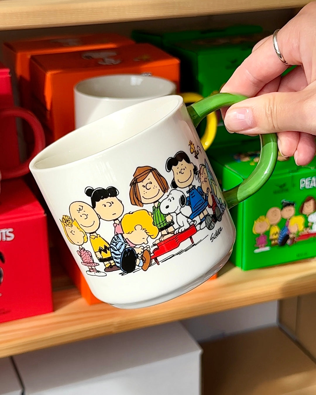 Official Peanuts® Gang ceramic mug with wraparound design featuring Snoopy, Charlie Brown, Woodstock, and friends; collectible coffee cup with green handle