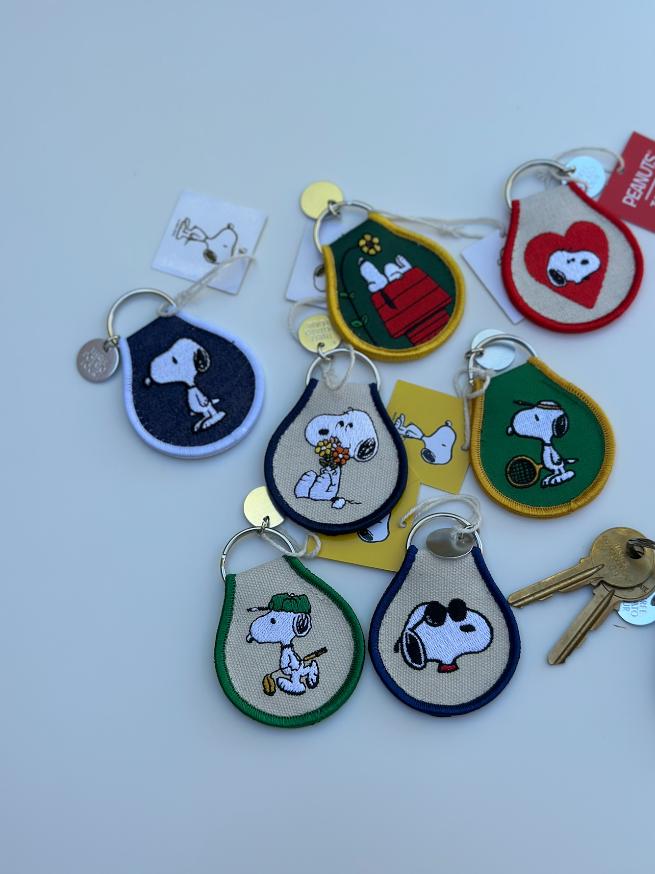 Assorted Peanuts® embroidered keychains displayed on a white table, including Snoopy flower bouquet design.