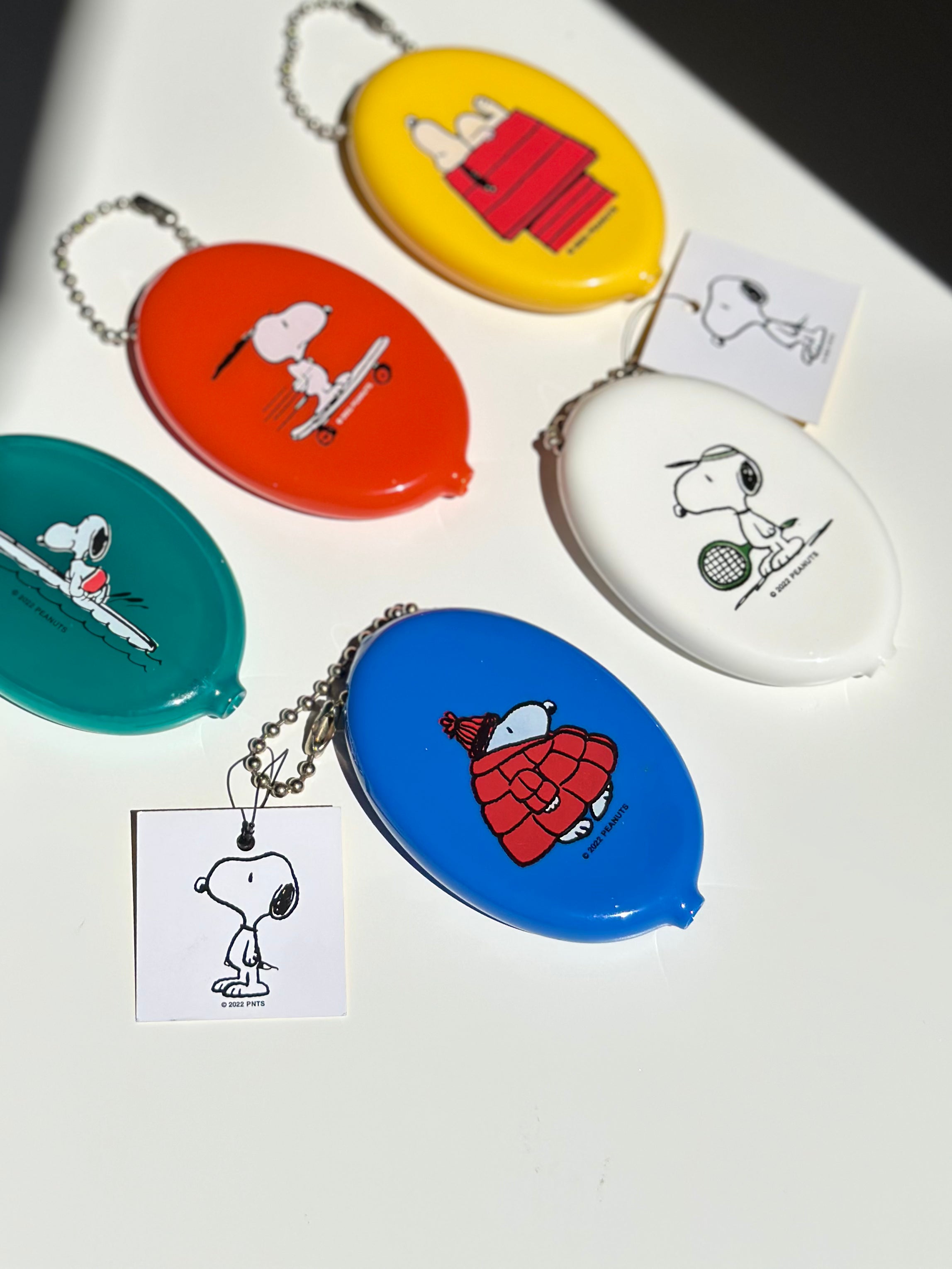 Set of colorful Snoopy coin pouch keychains featuring retro Peanuts® designs on blue, yellow, red, white, green, and orange vinyl.