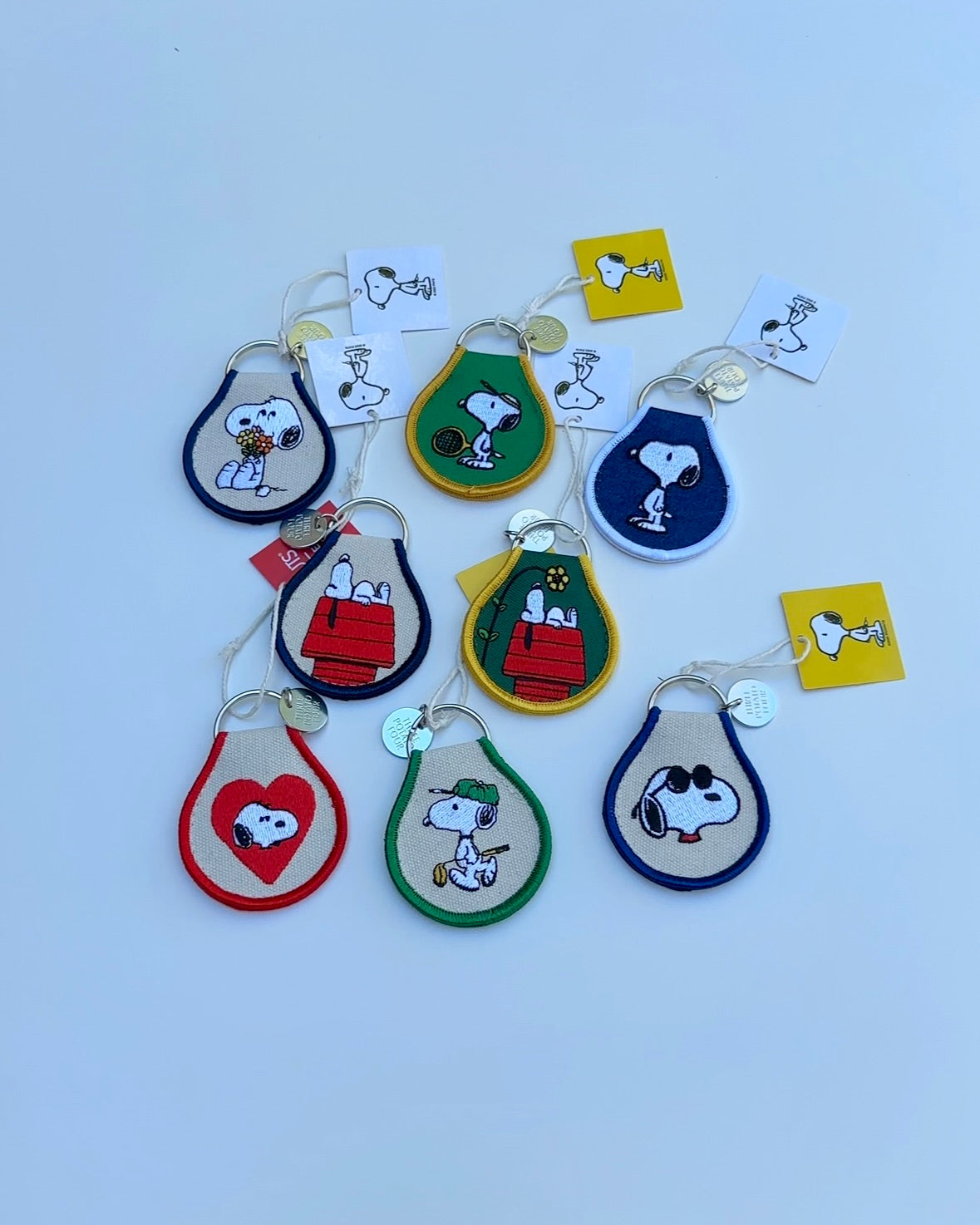 Flat lay of assorted Snoopy embroidered keychains, including Snoopy on a doghouse with yellow flower.