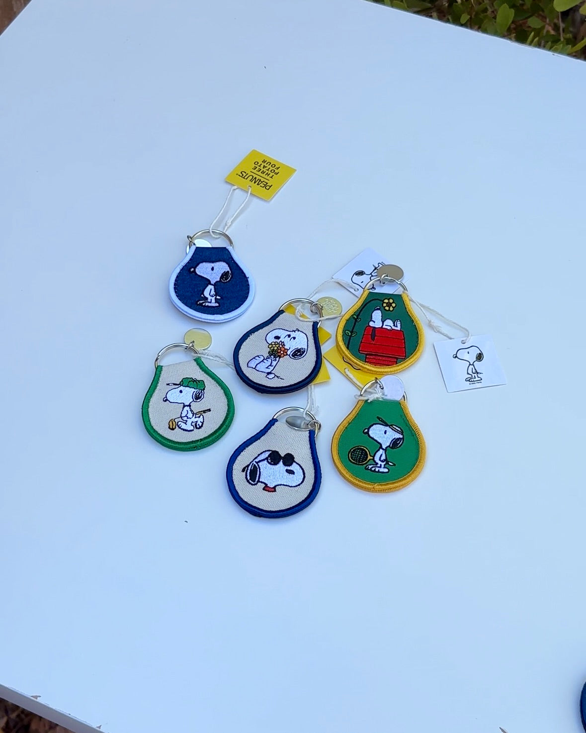 Group of Peanuts® embroidered keychains in various designs, including Snoopy on a doghouse with flower detail.