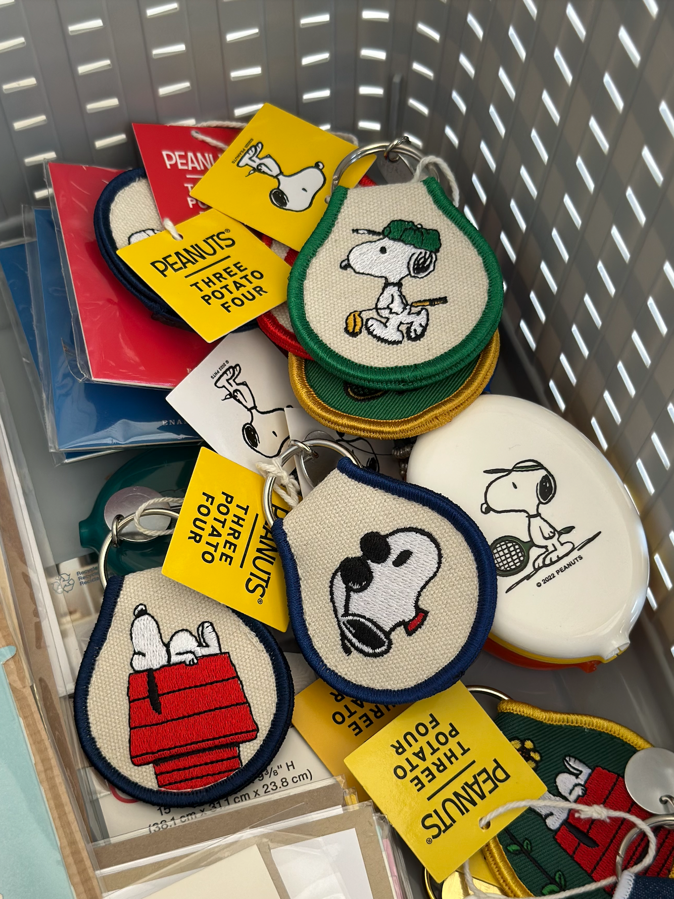 Basket filled with embroidered Snoopy keychains featuring doghouse, tennis, and sunglasses designs.