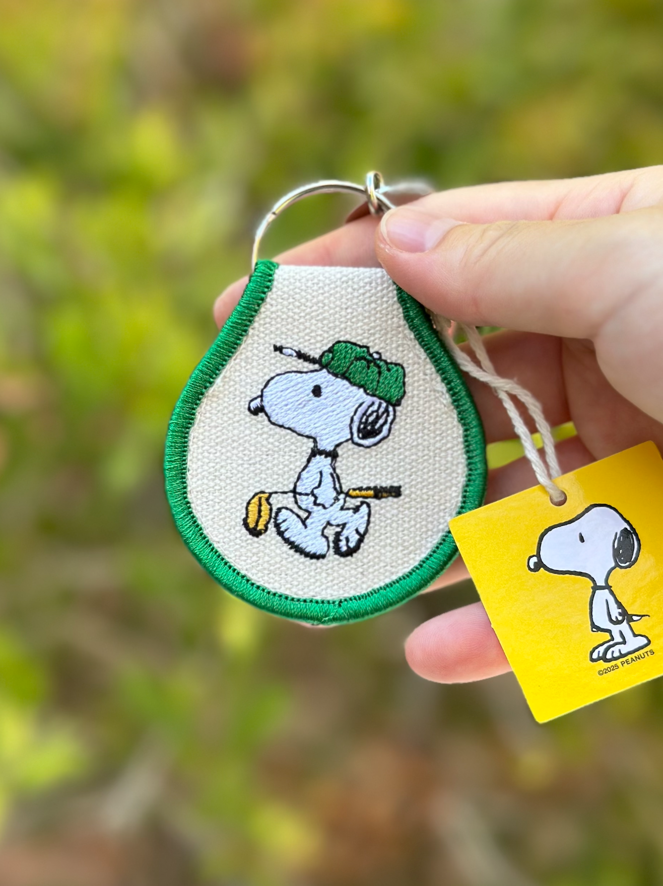 Close-up of Snoopy Peanuts double-sided embroidered golf keychain with green trim, officially licensed collectible made from oxford cotton.