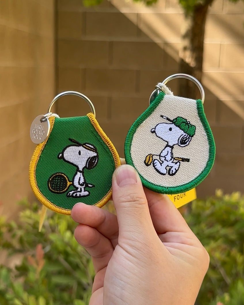Two Snoopy Peanuts embroidered golf keychains, one with green trim and one with yellow trim, featuring tennis and golfing Snoopy designs.