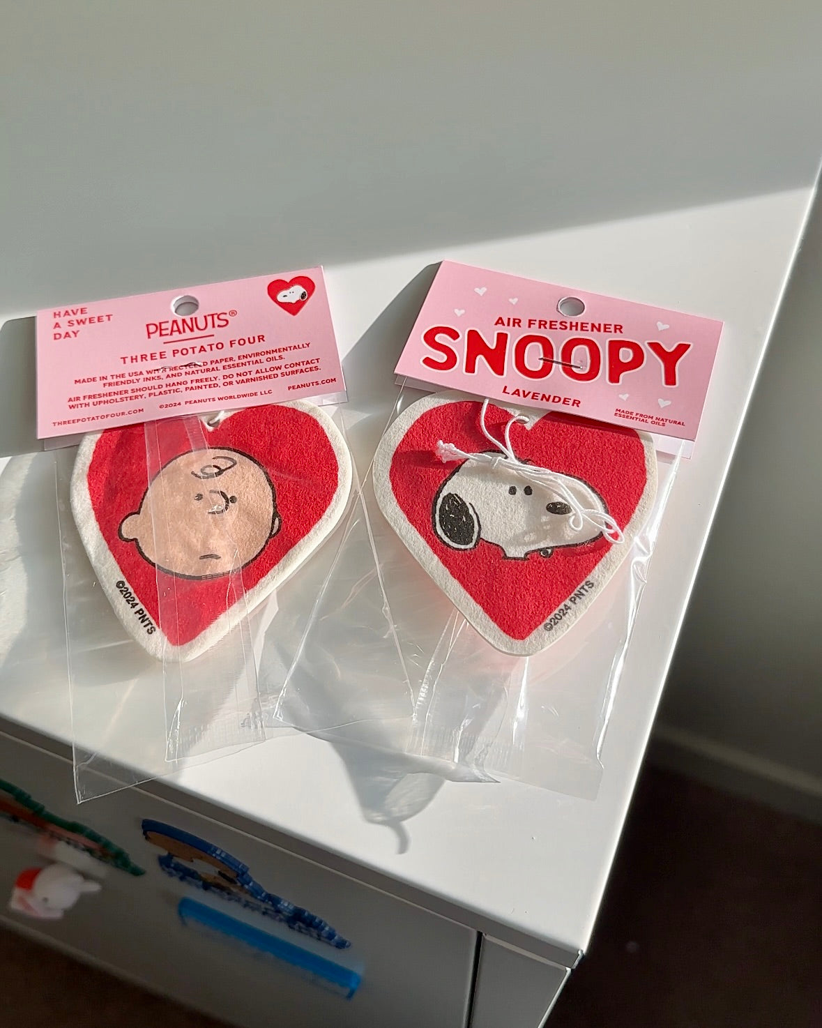 Front and back view of heart-shaped Snoopy air freshener with calming lavender scent. Features Snoopy on one side and Charlie Brown on the other. Cute car decor gift.