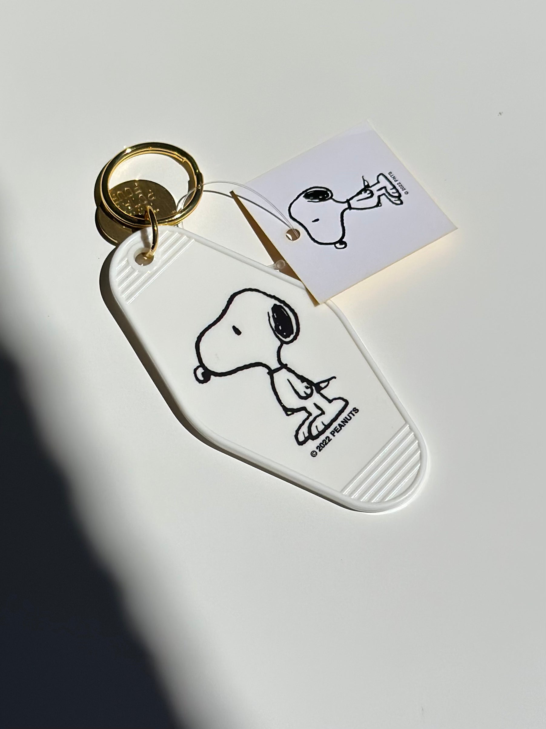 White acrylic motel keychain featuring Snoopy design with gold keyring.