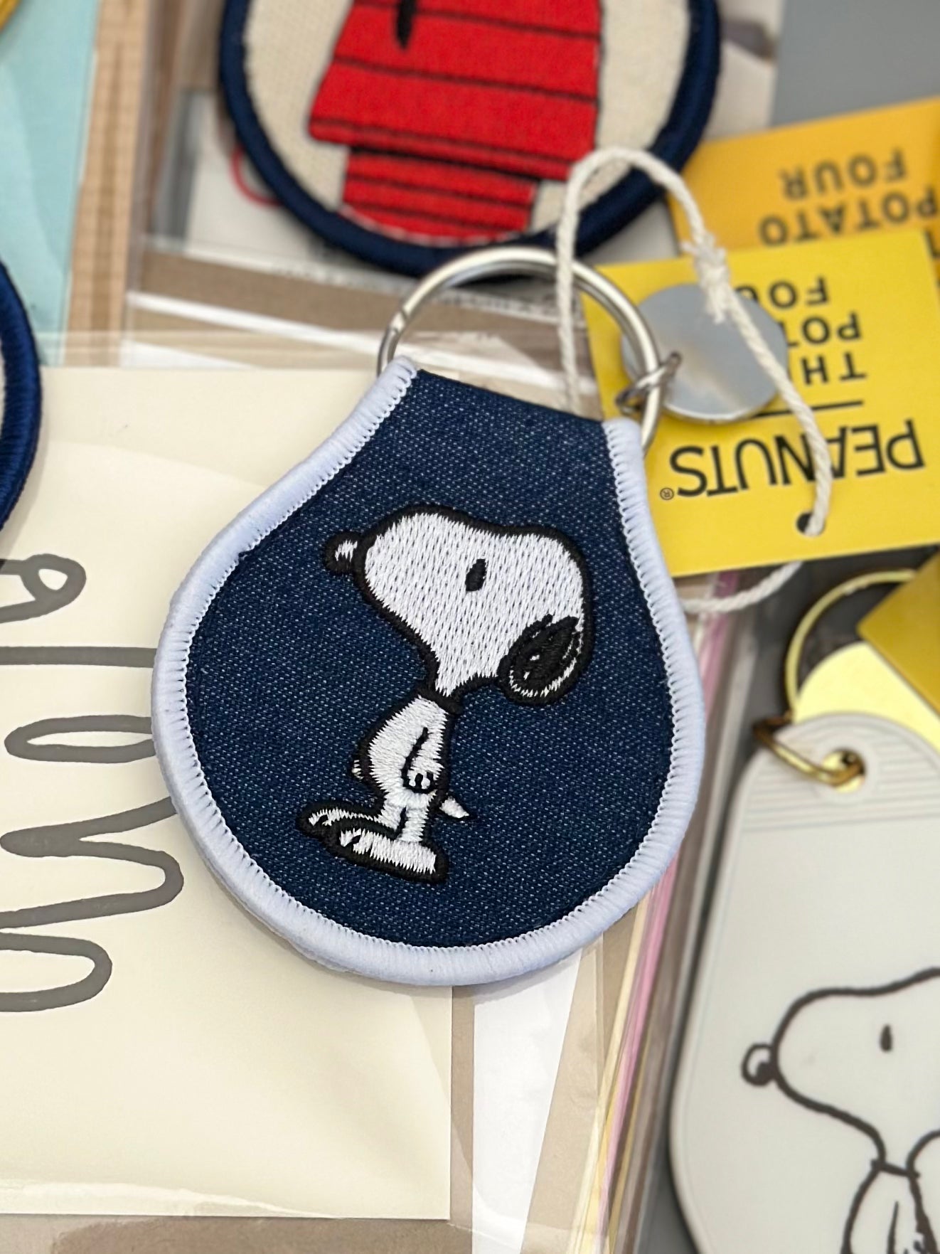 Embroidered Snoopy standing keychain on dark denim fabric with white trim.