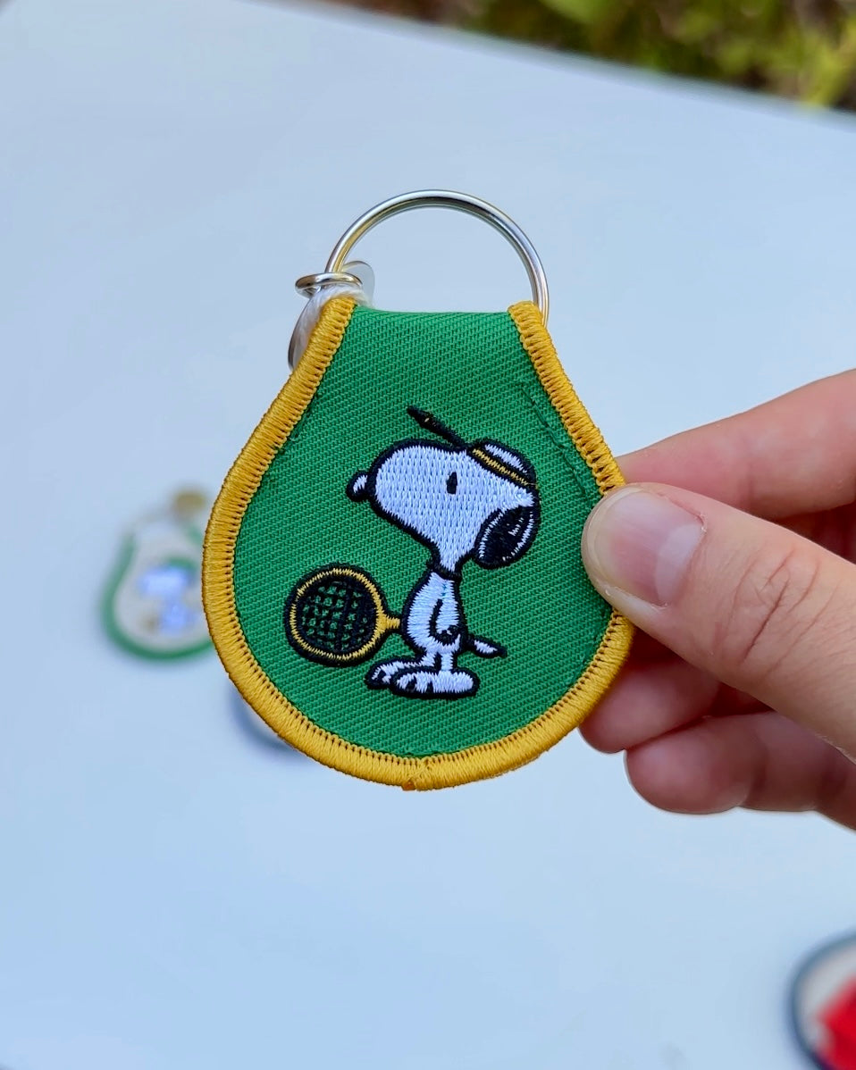Close-up of Snoopy Peanuts embroidered tennis keychain with yellow trim, officially licensed Peanuts collectible made from durable oxford cotton.