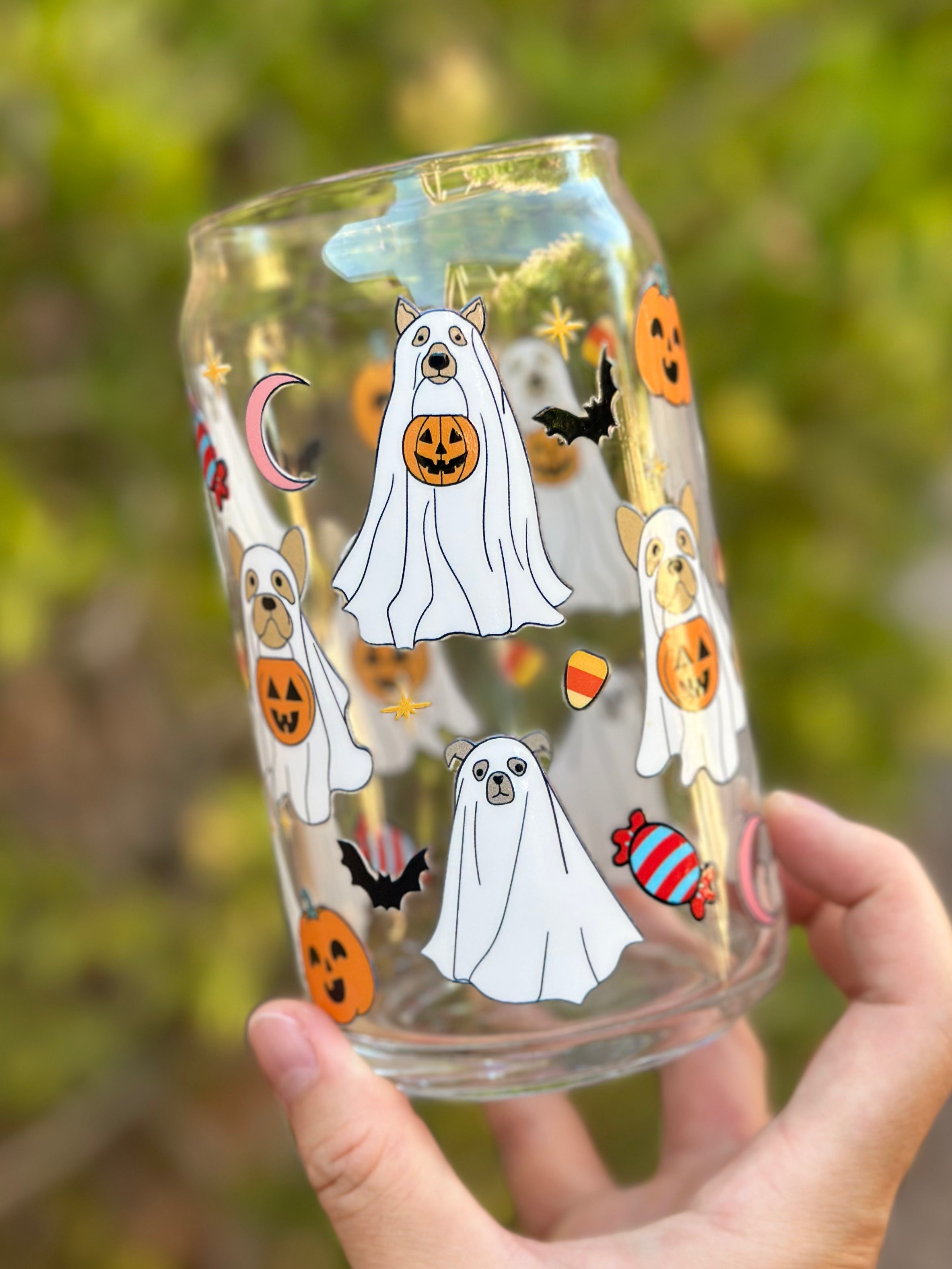 Halloween-themed glass can cup with dogs dressed as ghosts, holding jack-o’-lanterns, alongside bats, pumpkins, candy, and stars.