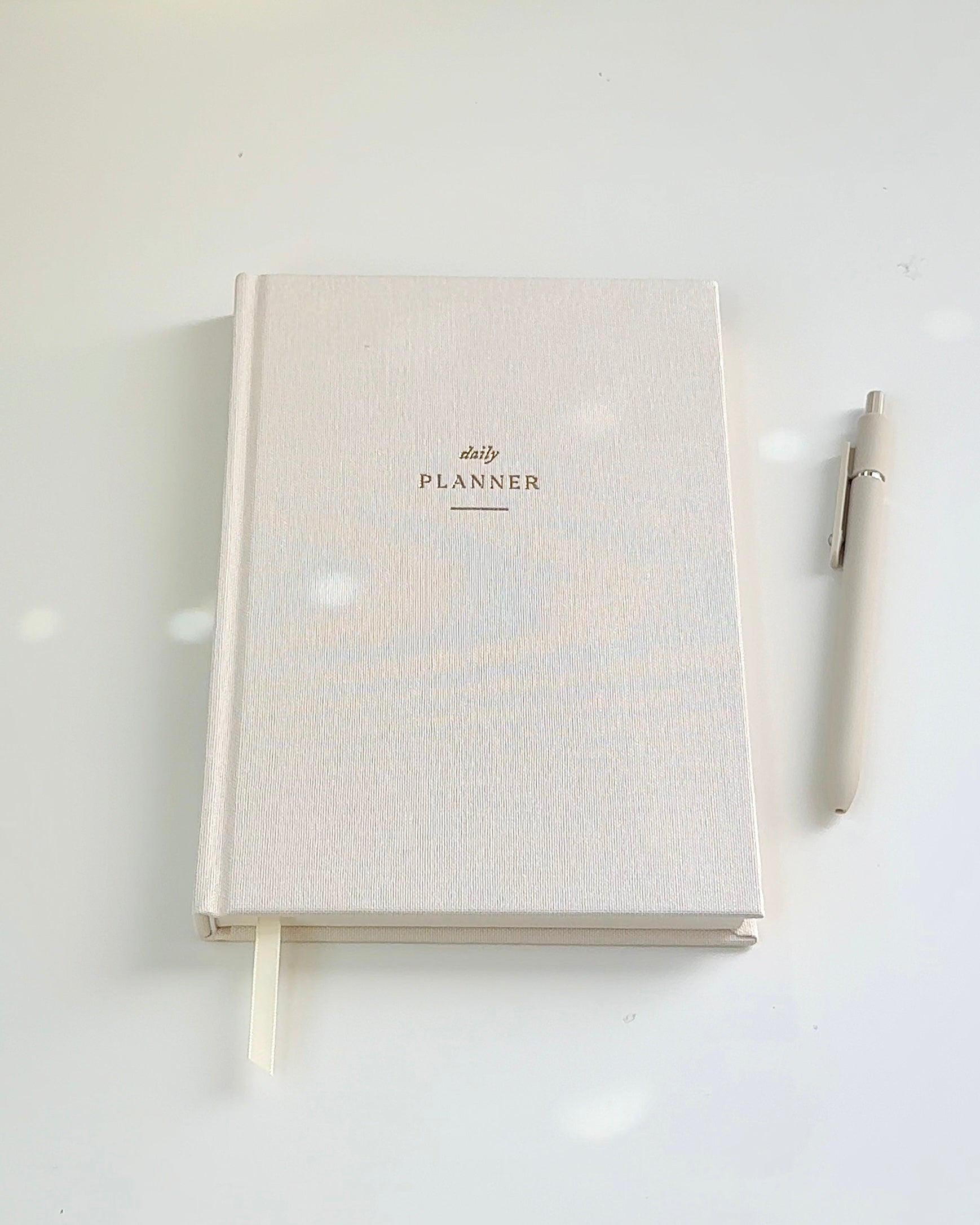 Undated beige linen daily planner with gold foil lettering on a white desk – aesthetic soft girl journal for summer productivity and gentle routine building