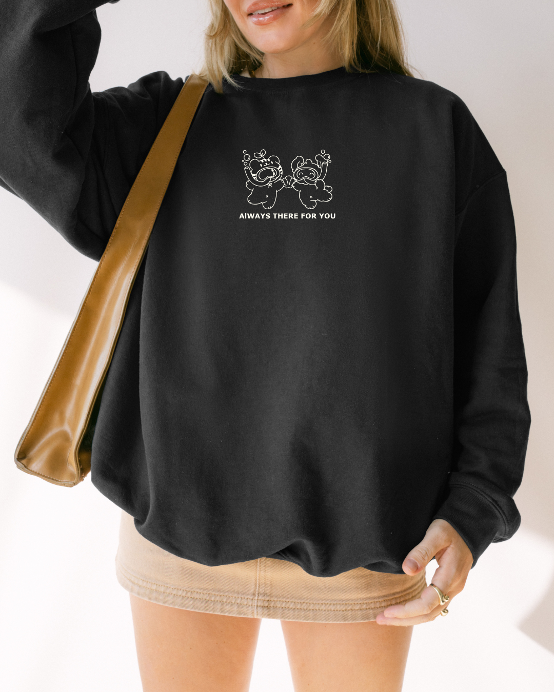 Close-up of a black oversized crewneck sweatshirt with white embroidered characters and the text “always there for you”
