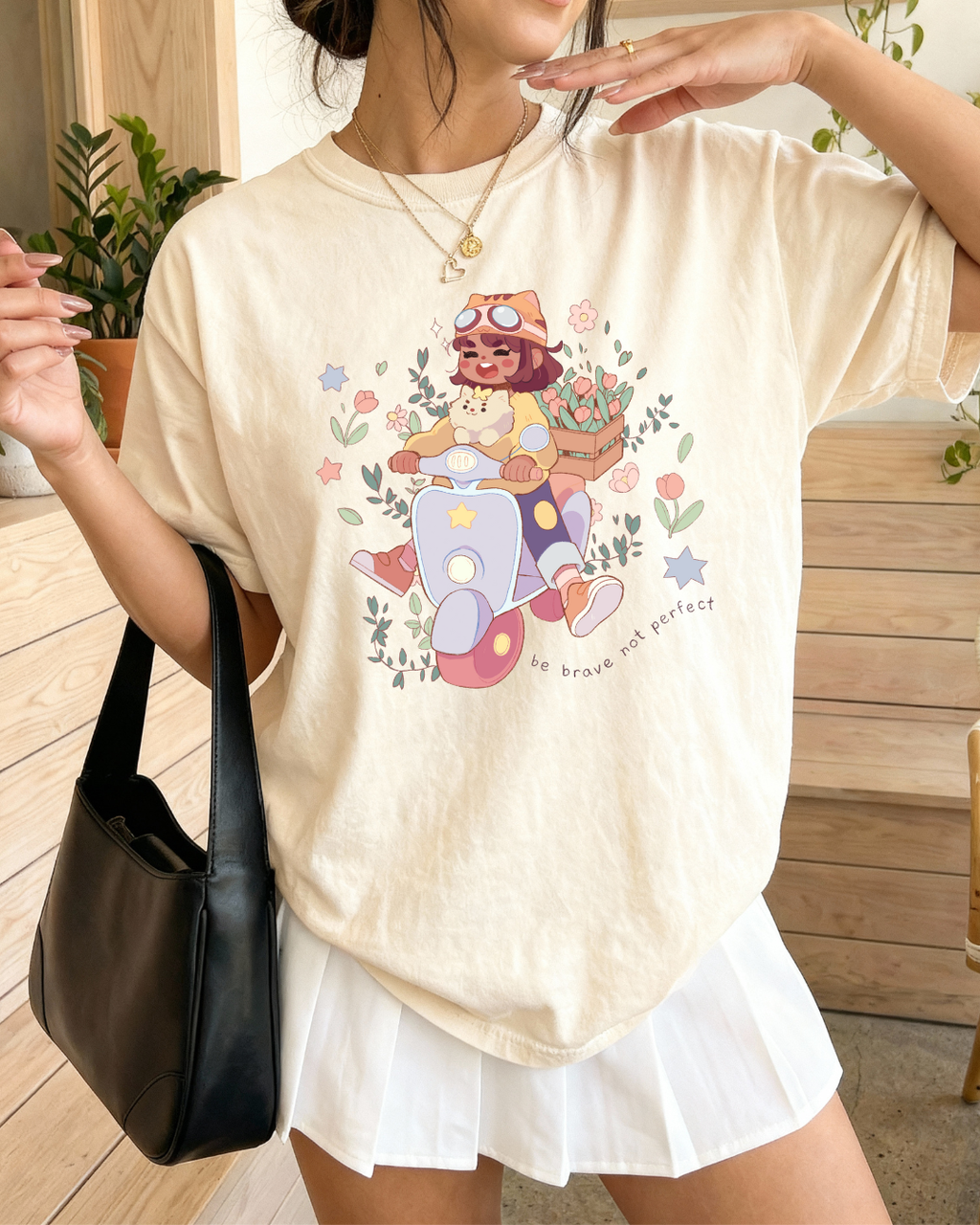 Ivory graphic t shirt featuring a soft illustrated design of a girl and her dog riding a scooter with flowers and the phrase "Be brave not perfect," styled for a gentle motivational look