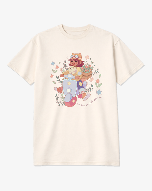 Ivory unisex graphic tee featuring a whimsical illustration of a girl riding a scooter with her dog and the phrase “Be Brave, Not Perfect,” a soft motivational shirt for creatives and overthinkers.