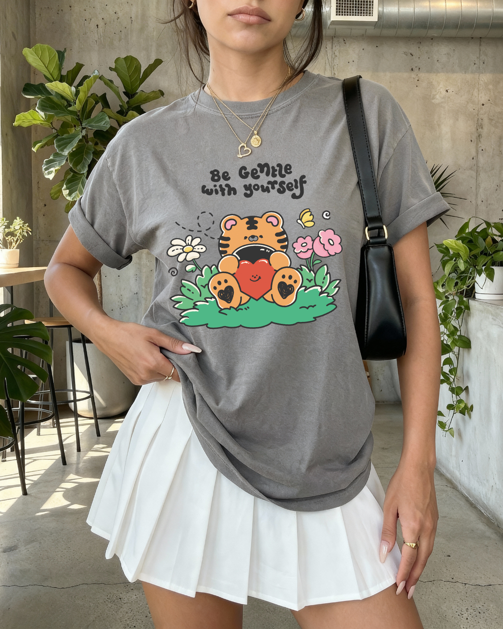 Charcoal gray graphic tee with a sweet tiger illustration and the phrase “be gentle with yourself,” worn indoors in a cozy setting