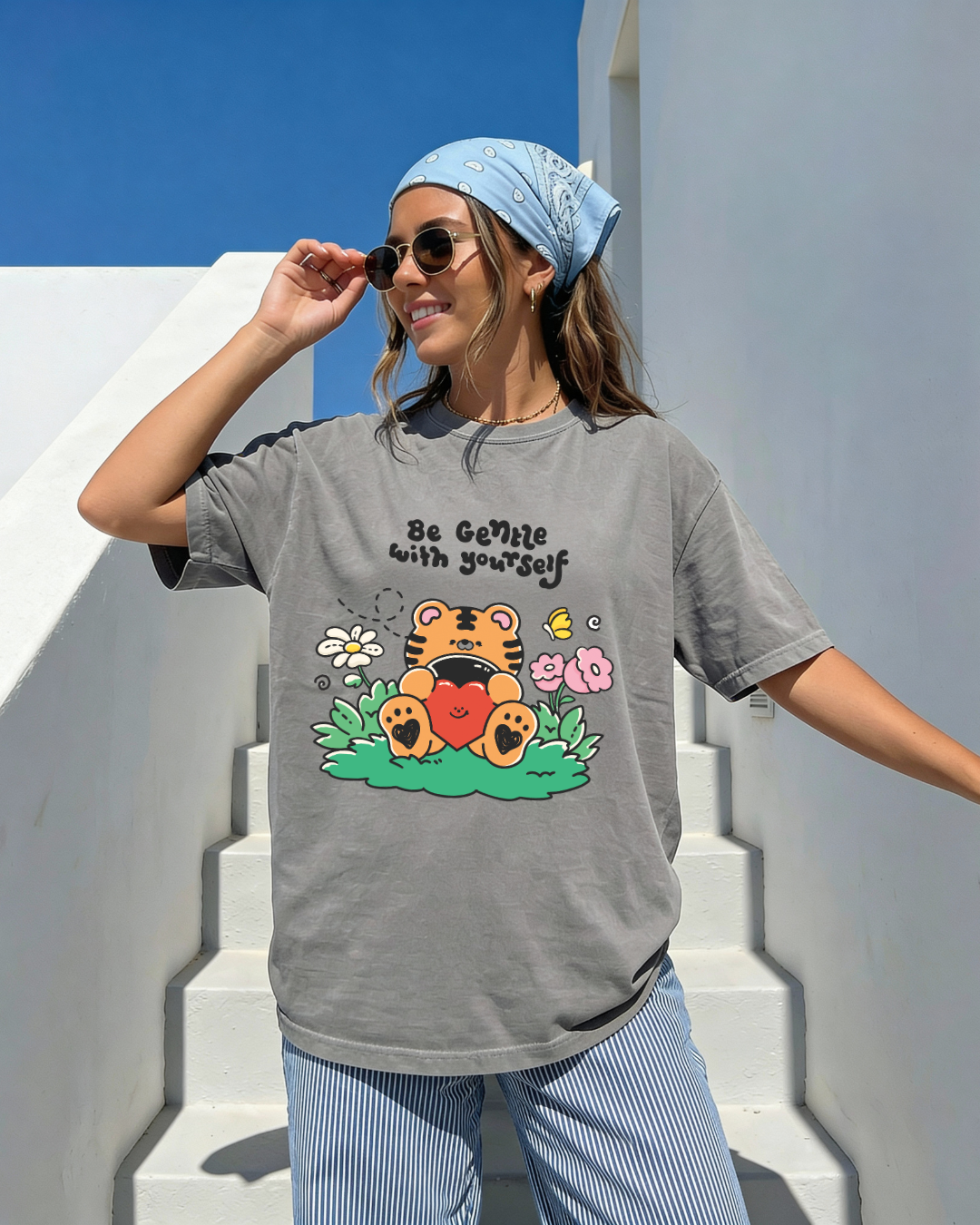 Woman wearing a charcoal gray “be gentle with yourself” graphic tee with a cute tiger illustration outdoors in bright sunlight