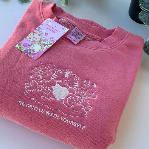 Close-up of embroidered tiger and floral design on a rose pink sweatshirt with “Be Gentle With Yourself” stitched below