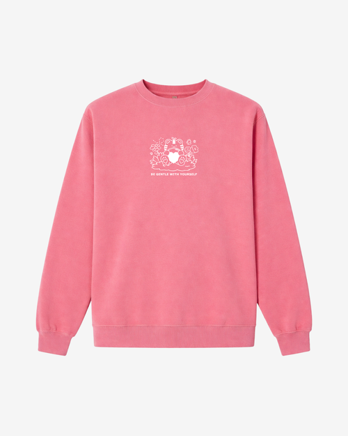 pink crewneck sweatshirt featuring subtle white embroidery of a gentle character holding a heart with the words “Be Gentle With Yourself” on the front.