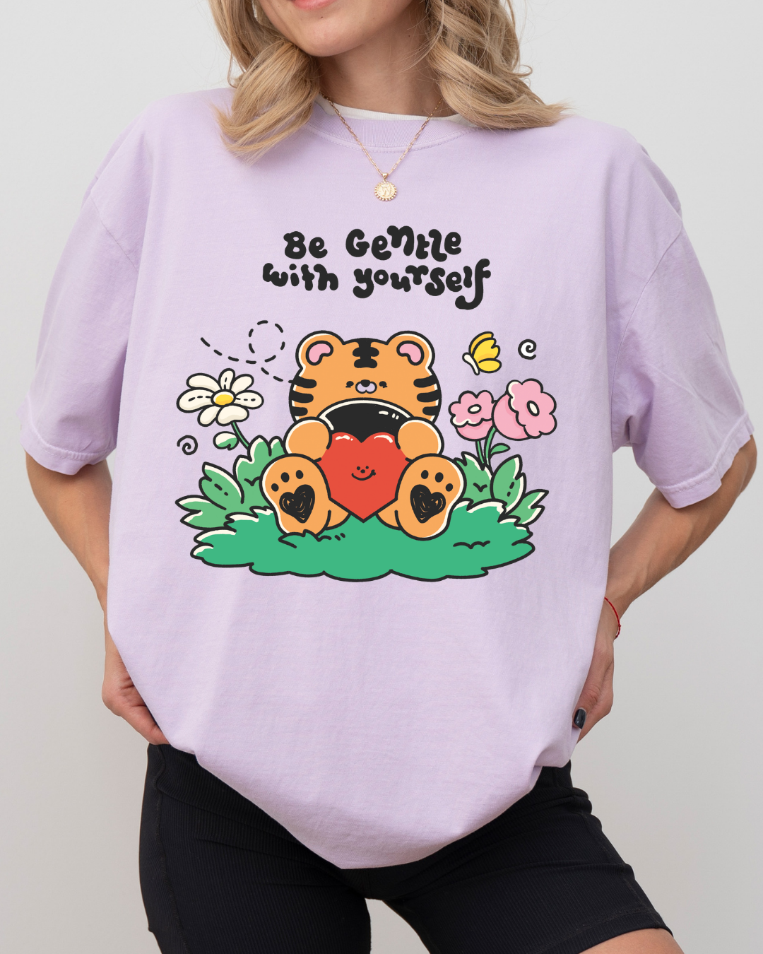 Pastel purple graphic t-shirt featuring a cute tiger hugging a heart with the phrase “be gentle with yourself”