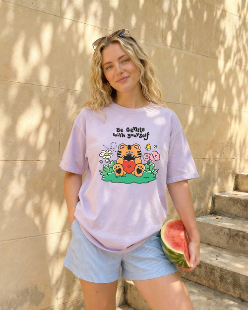 Person wearing a pastel purple “be gentle with yourself” graphic t-shirt styled casually outdoors