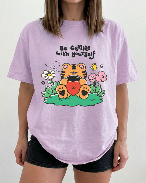 Close-up of the “be gentle with yourself” tiger illustration printed on a pastel purple t-shirt