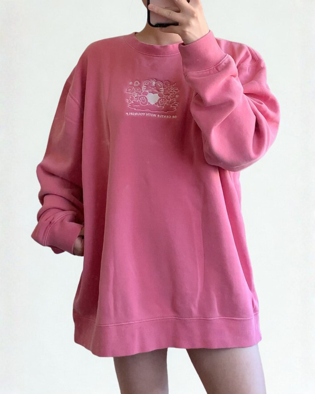 Oversized rose pink embroidered sweatshirt worn casually, featuring a gentle self care message and minimalist tiger embroidery