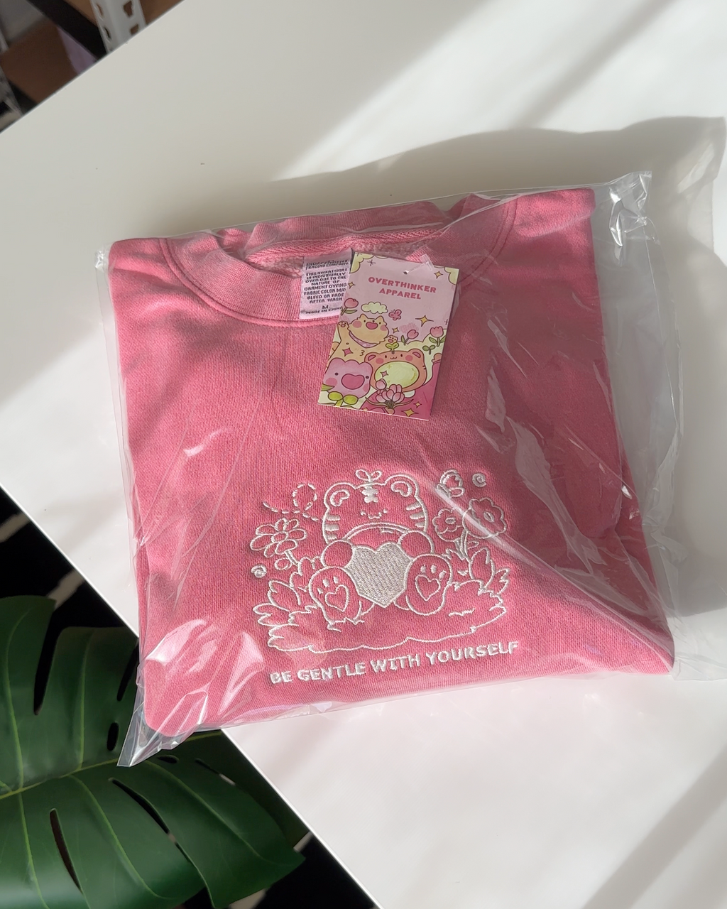 Rose pink embroidered sweatshirt packaged and ready to ship, featuring a calming self care message and tiger design