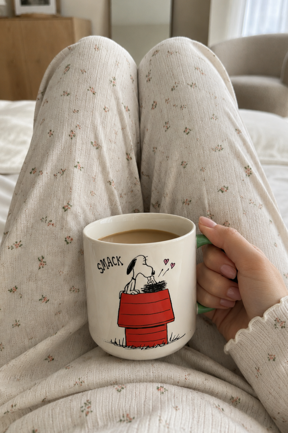 Woman relaxing in bed holding a Snoopy Be Kind to All Kinds ceramic mug filled with coffee during a calm morning routine.
