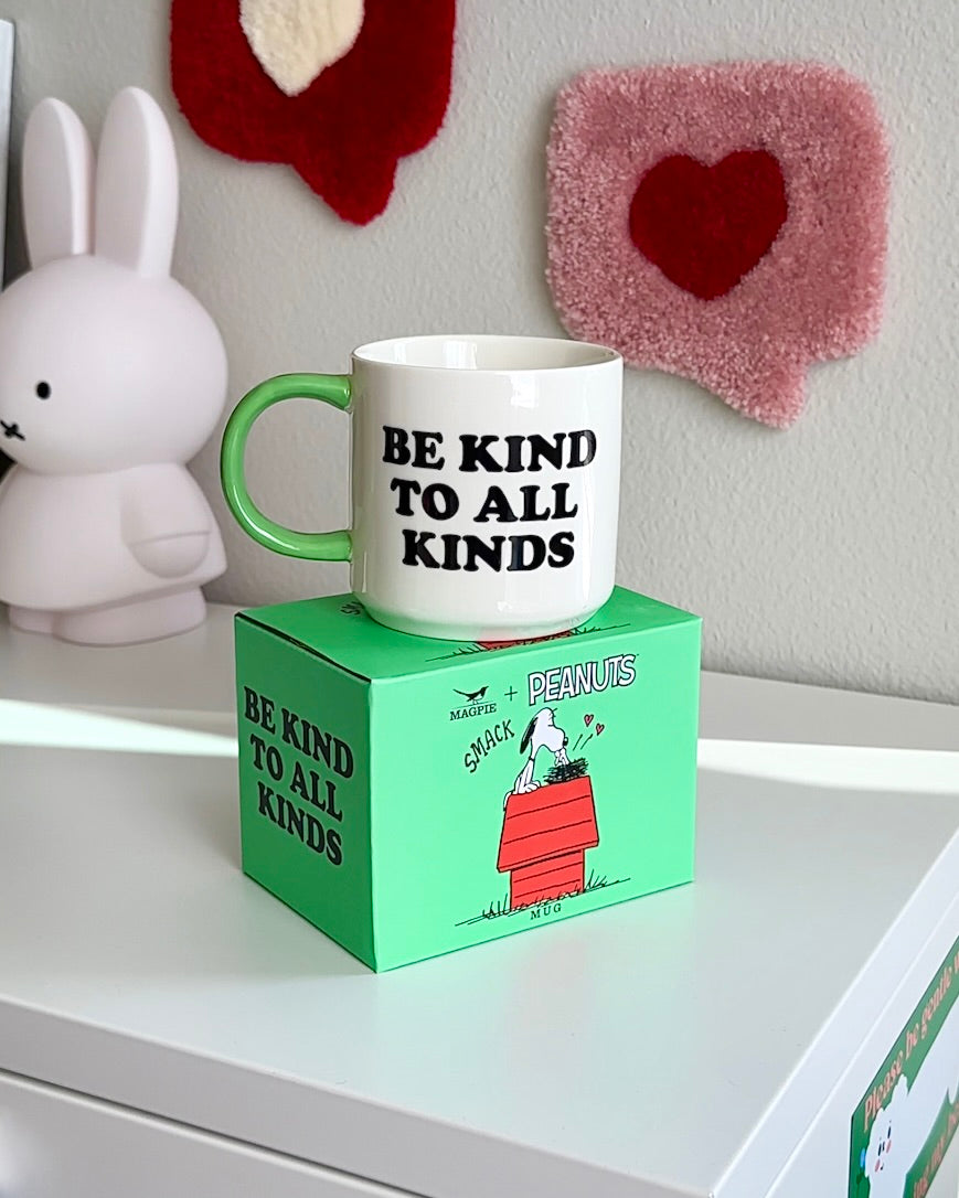 Snoopy “Be Kind to All Kinds” coffee mug displayed on its Peanuts collector box, white mug with green handle and kindness message, giftable ceramic mug.