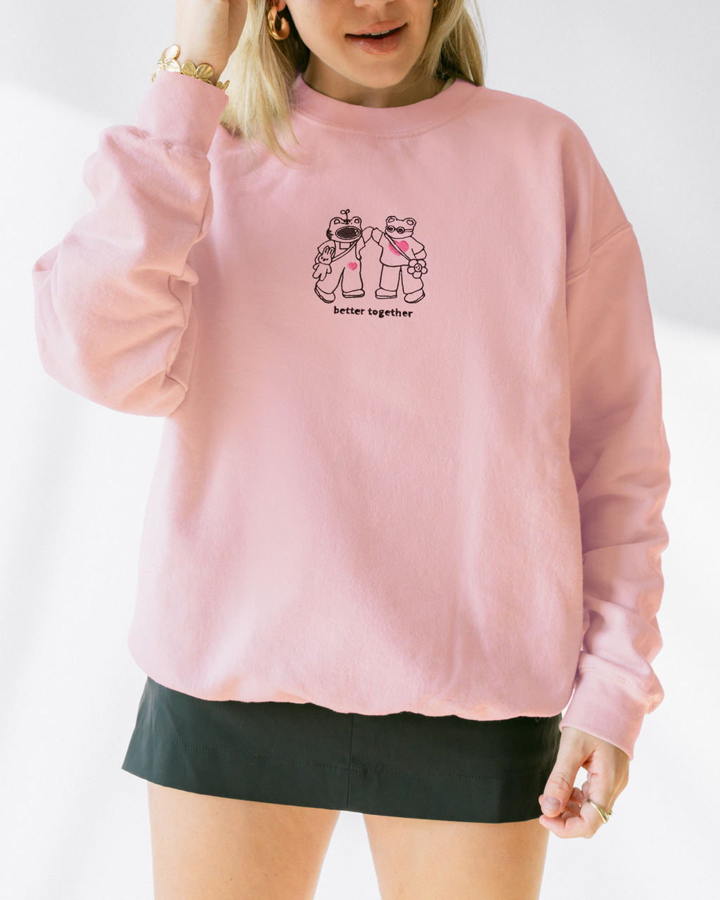 Model wearing a soft pink embroidered “Better Together” sweatshirt featuring two characters holding hands.