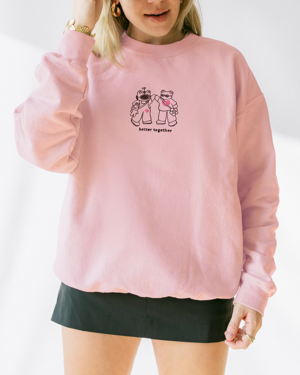 Model wearing a soft pink embroidered “Better Together” sweatshirt featuring two characters holding hands.