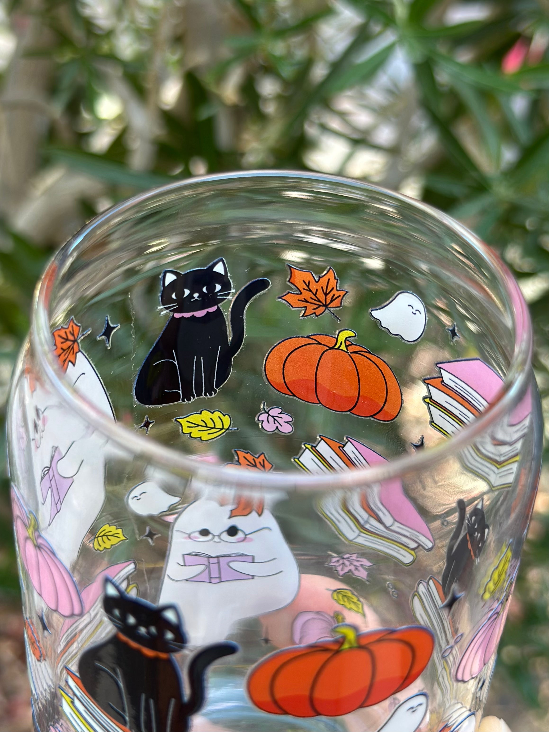 Inside top view of black cat, pumpkins, ghosts, and books on a clear glass can cup.