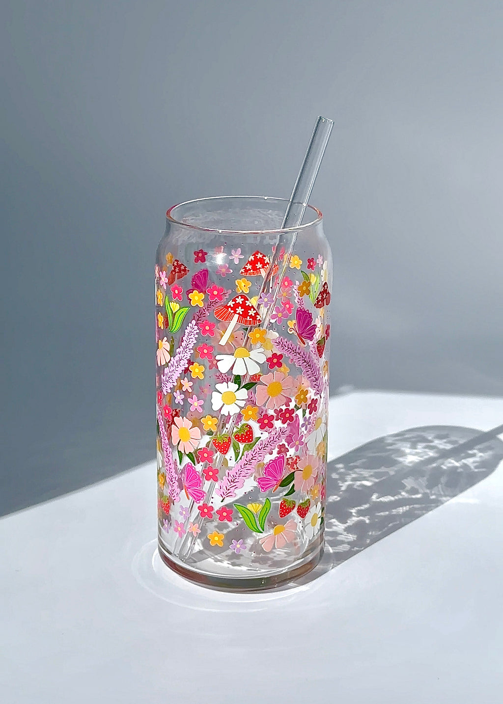 20 oz blooming garden glass can with a reusable glass straw, featuring bright floral cottagecore artwork with wildflowers, strawberries, mushrooms, and butterflies.