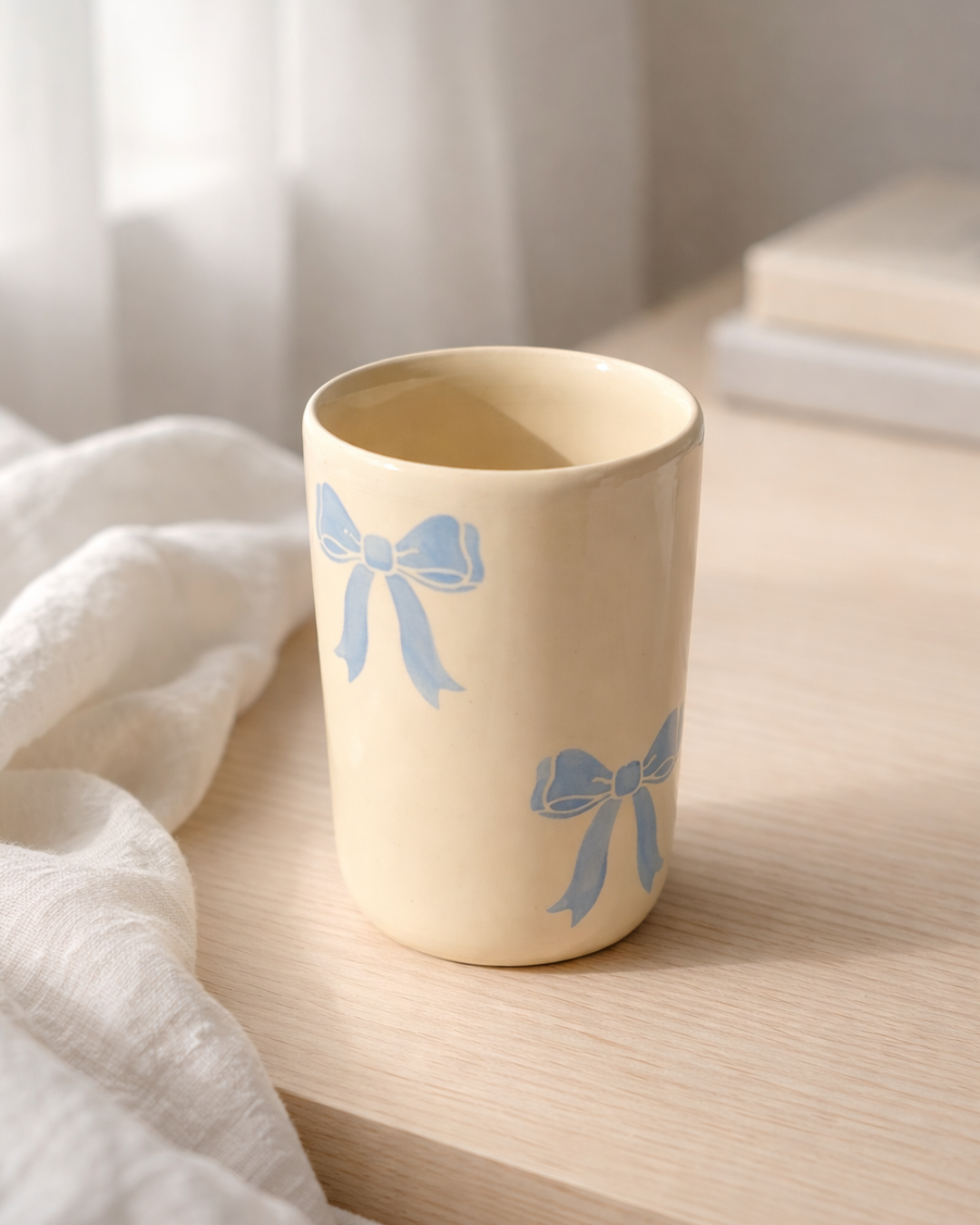 Handmade ceramic coffee mug with blue bow design on a wooden table, aesthetic ceramic bow mug for cozy coffee rituals and feminine kitchen decor
