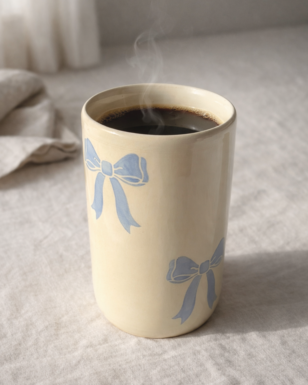 Handmade ceramic coffee mug with blue bow design filled with hot coffee, aesthetic bow mug for cozy coffee rituals and coffee bar decor