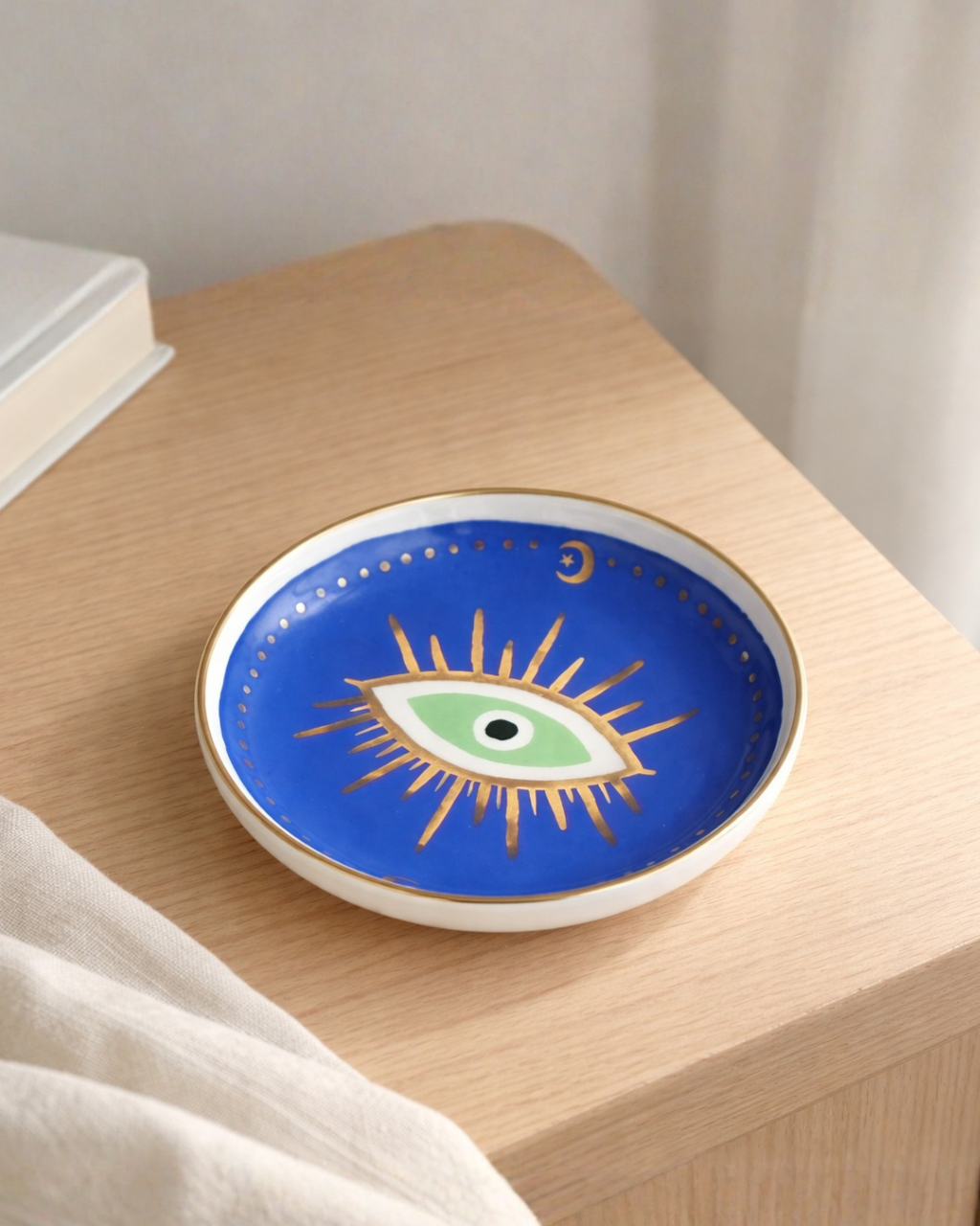 Blue evil eye trinket dish on wooden bedside table, decorative ring holder tray for nightstand decor and small jewelry storage