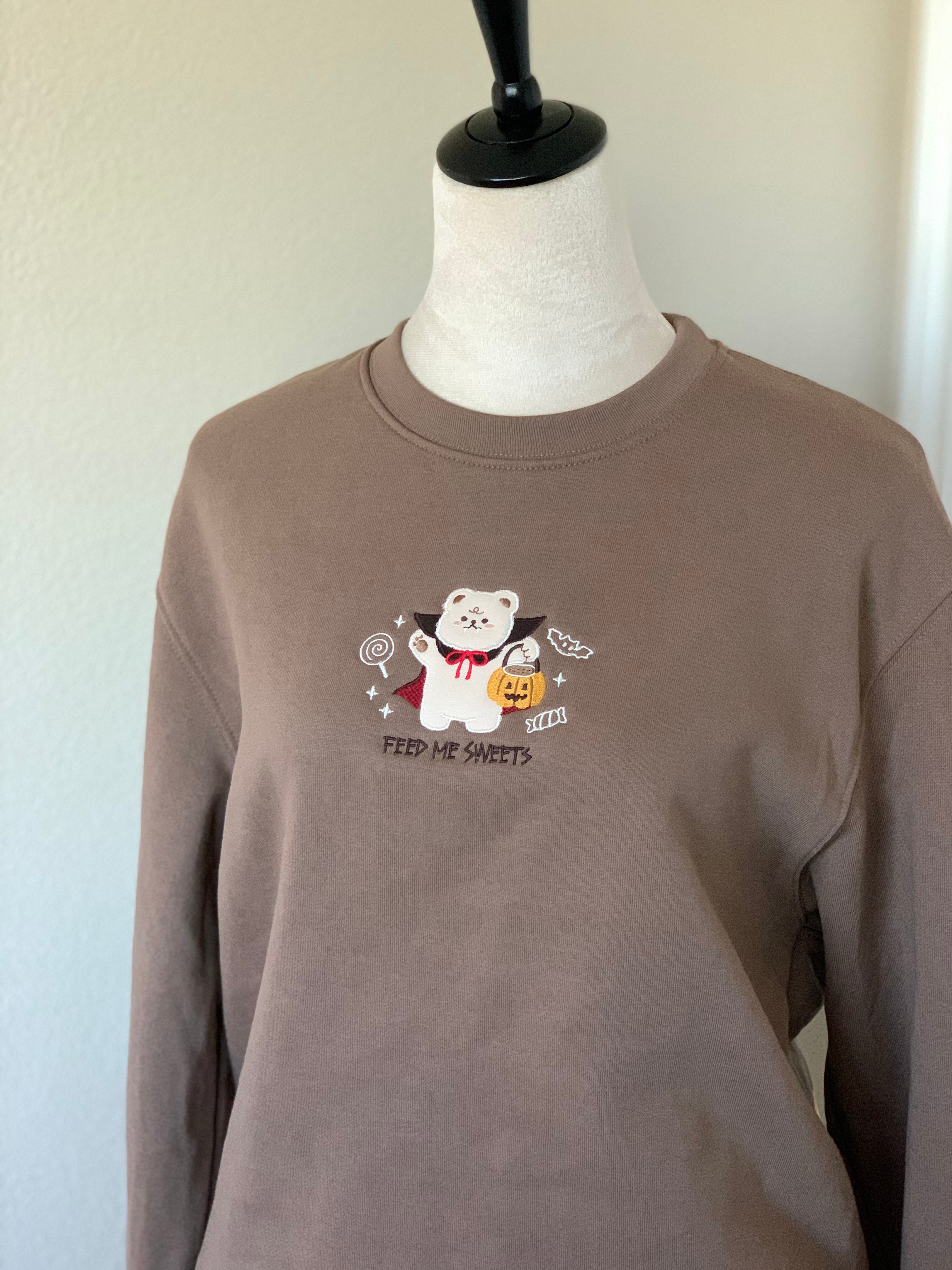 Angled view of brown embroidered sweatshirt with vampire bear and Halloween candy design.