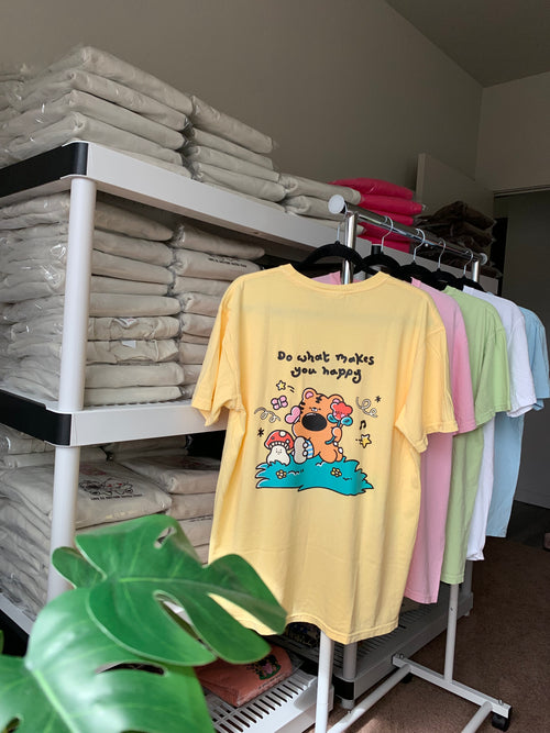 Butter yellow graphic t shirt with cute illustrated back design hanging on rack in small batch studio