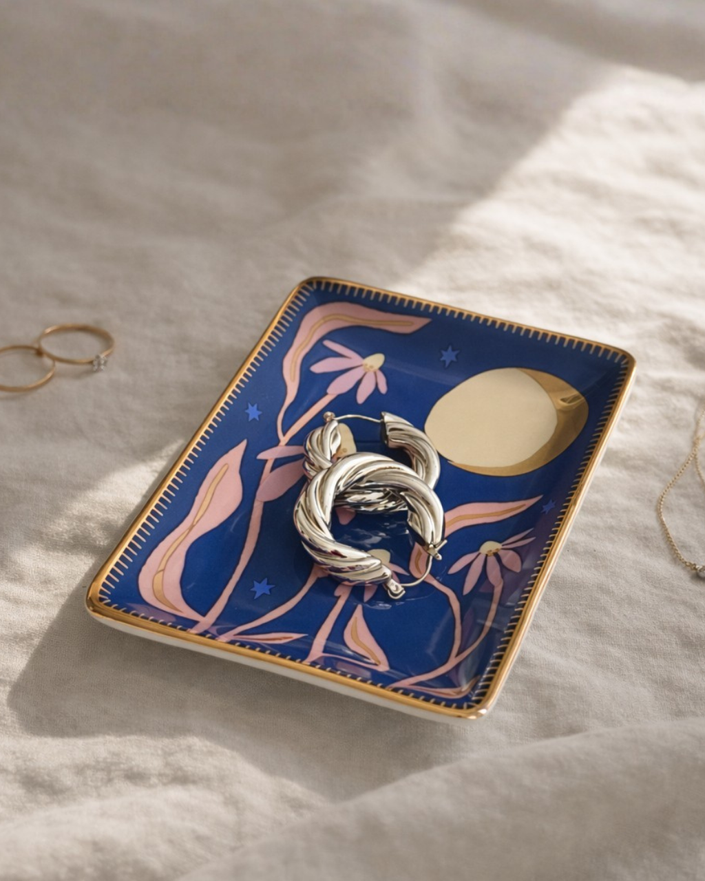 Blue celestial floral jewelry tray with gold moon and pink flowers holding silver hoop earrings, decorative trinket dish for rings earrings and small jewelry