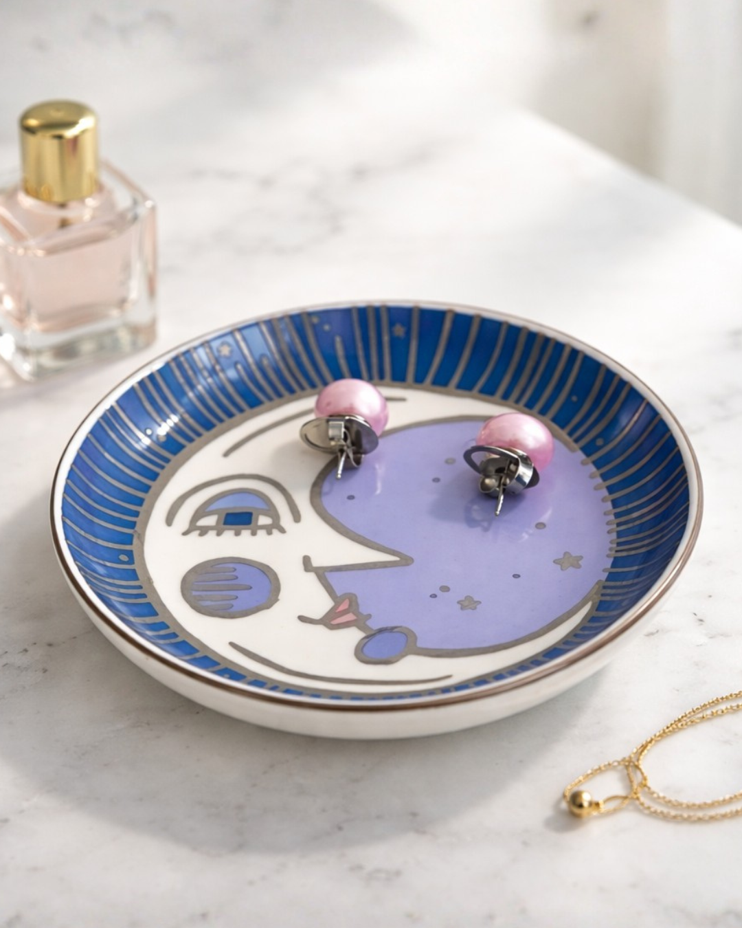 Celestial moon face ring holder dish on marble vanity surface with perfume bottle and gold necklace, decorative jewelry organizer tray