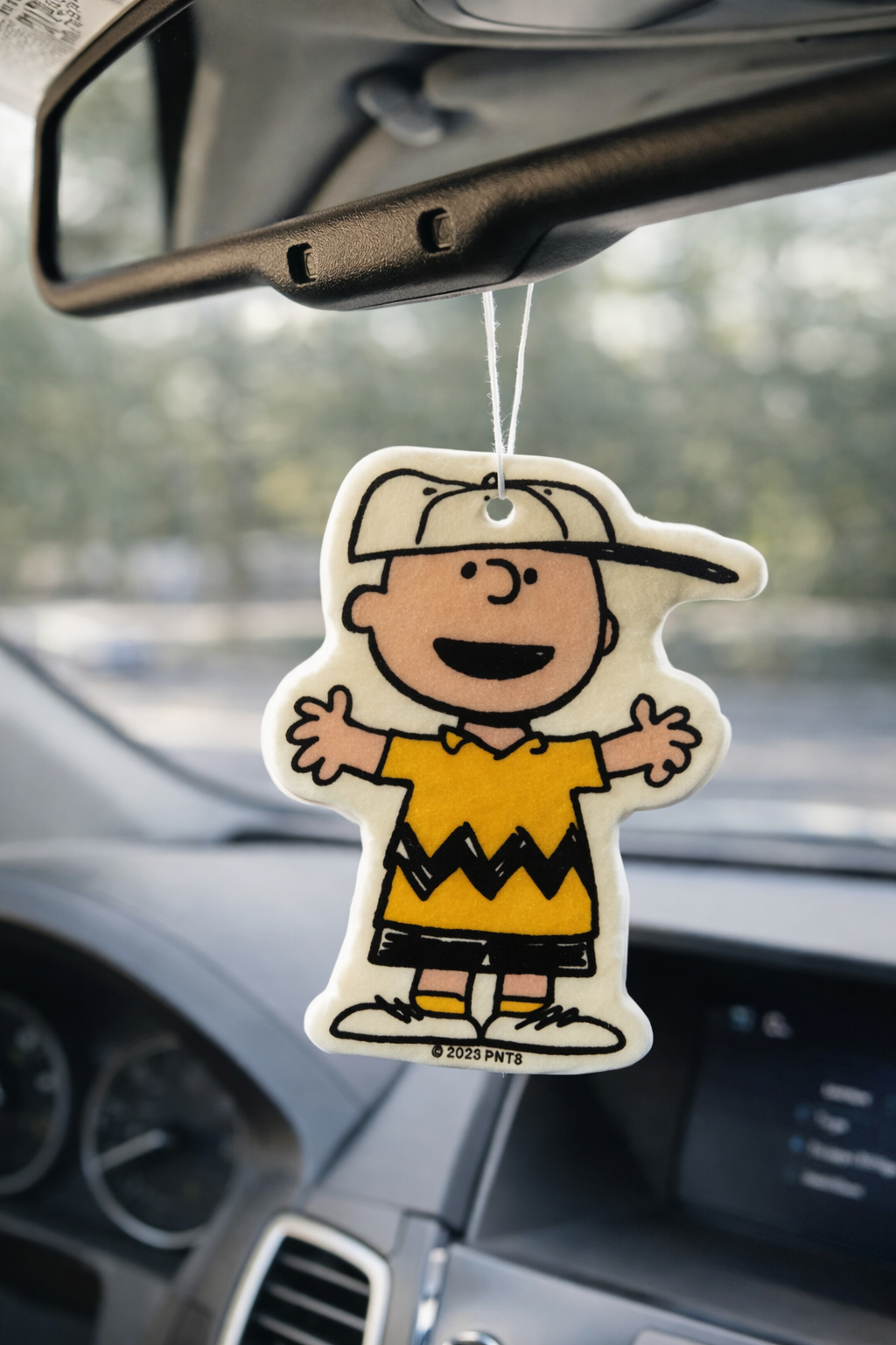Charlie Brown car air freshener hanging from rearview mirror, cute Peanuts car decor accessory.