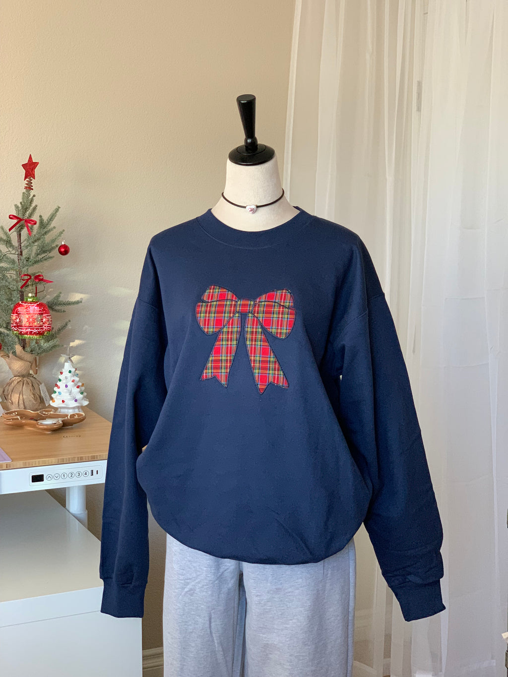 Centered view of plaid bow graphic on navy sweatshirt in bright natural light