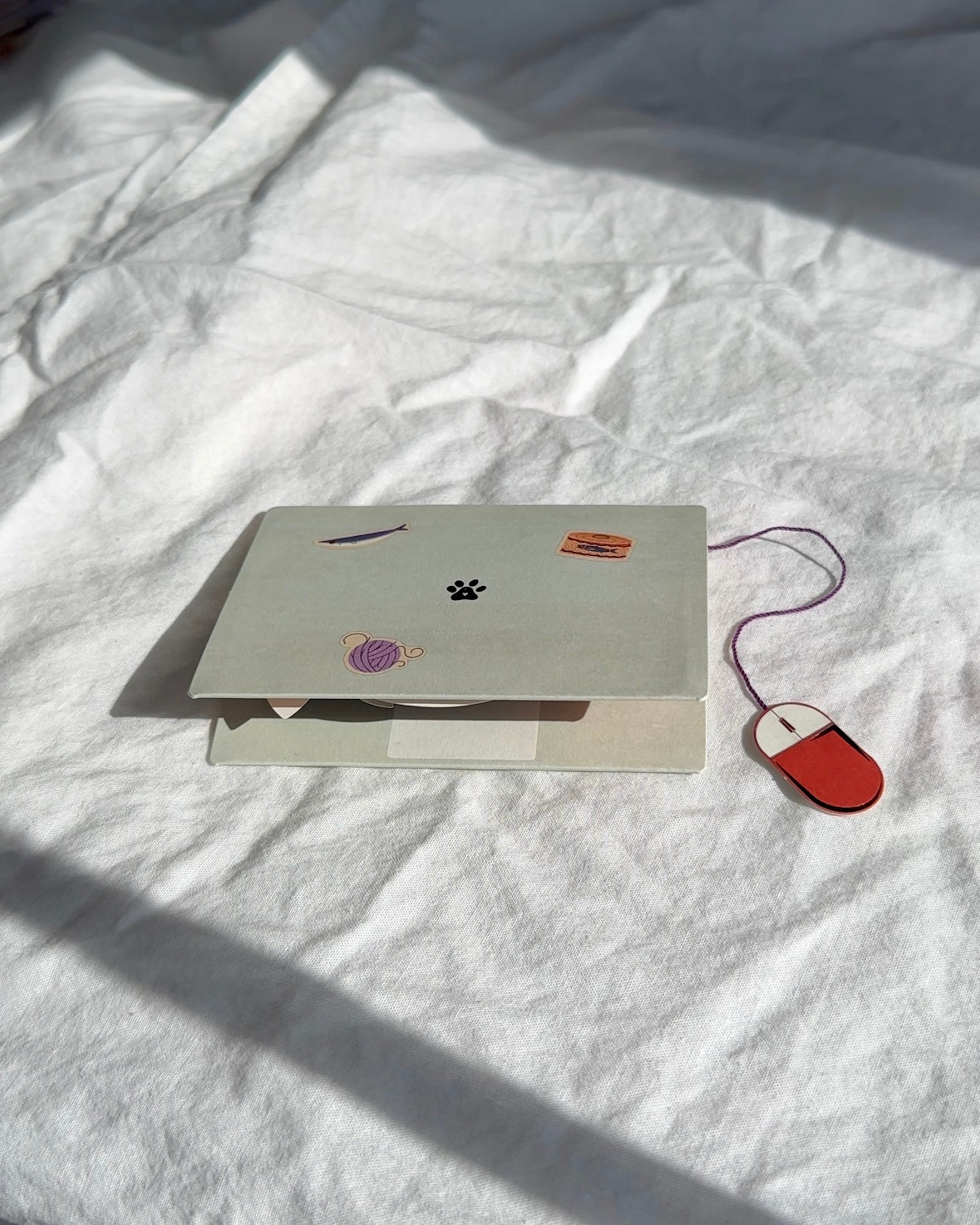 Closed cat pop-up card designed like a laptop with fish, paw print, and yarn illustrations.